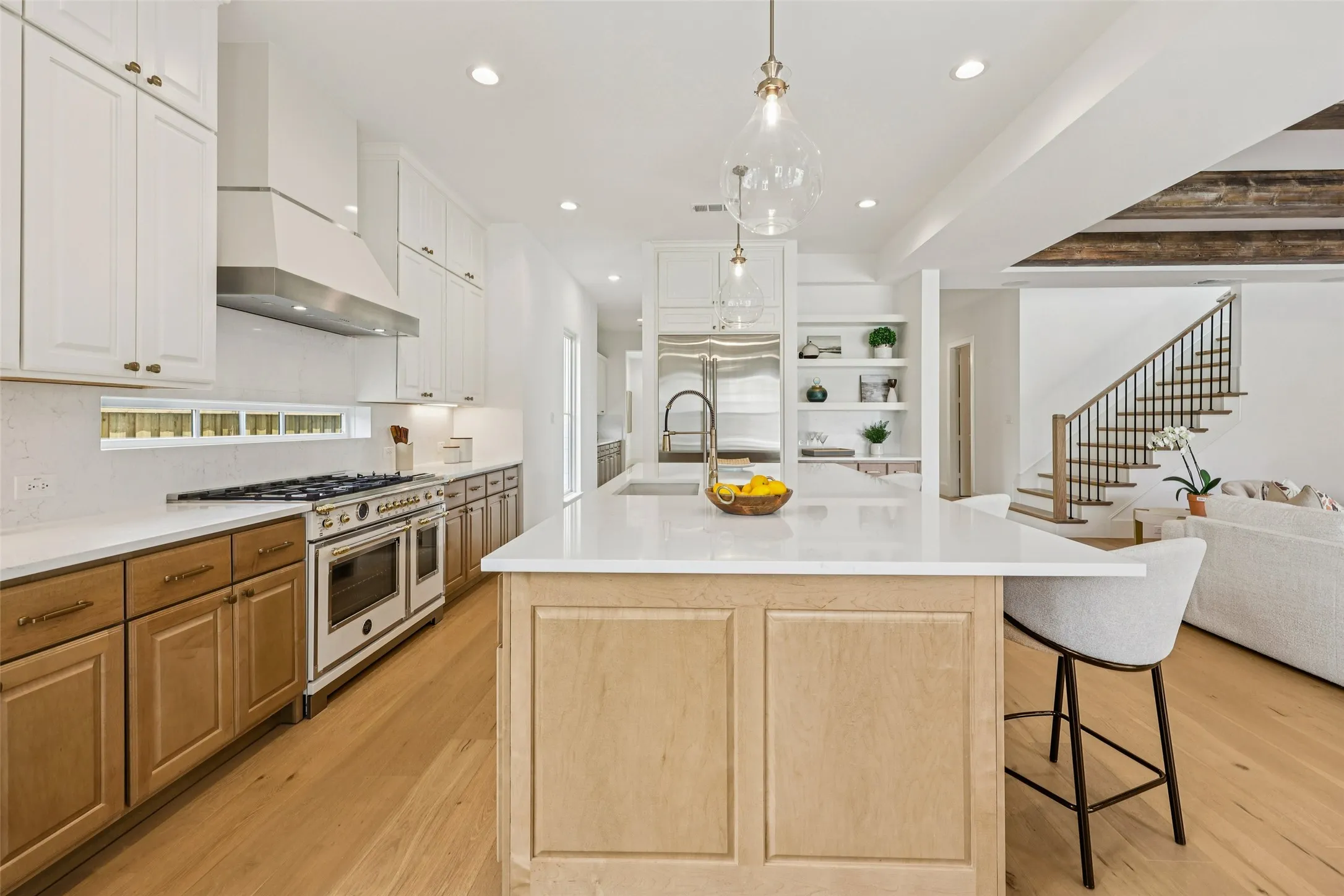 Gourmet kitchen with wood-finish flooring, a central island featuring a stainless steel sink and pendant lighting, a built-in range with a stainless steel hood, and two-tone cabinetry