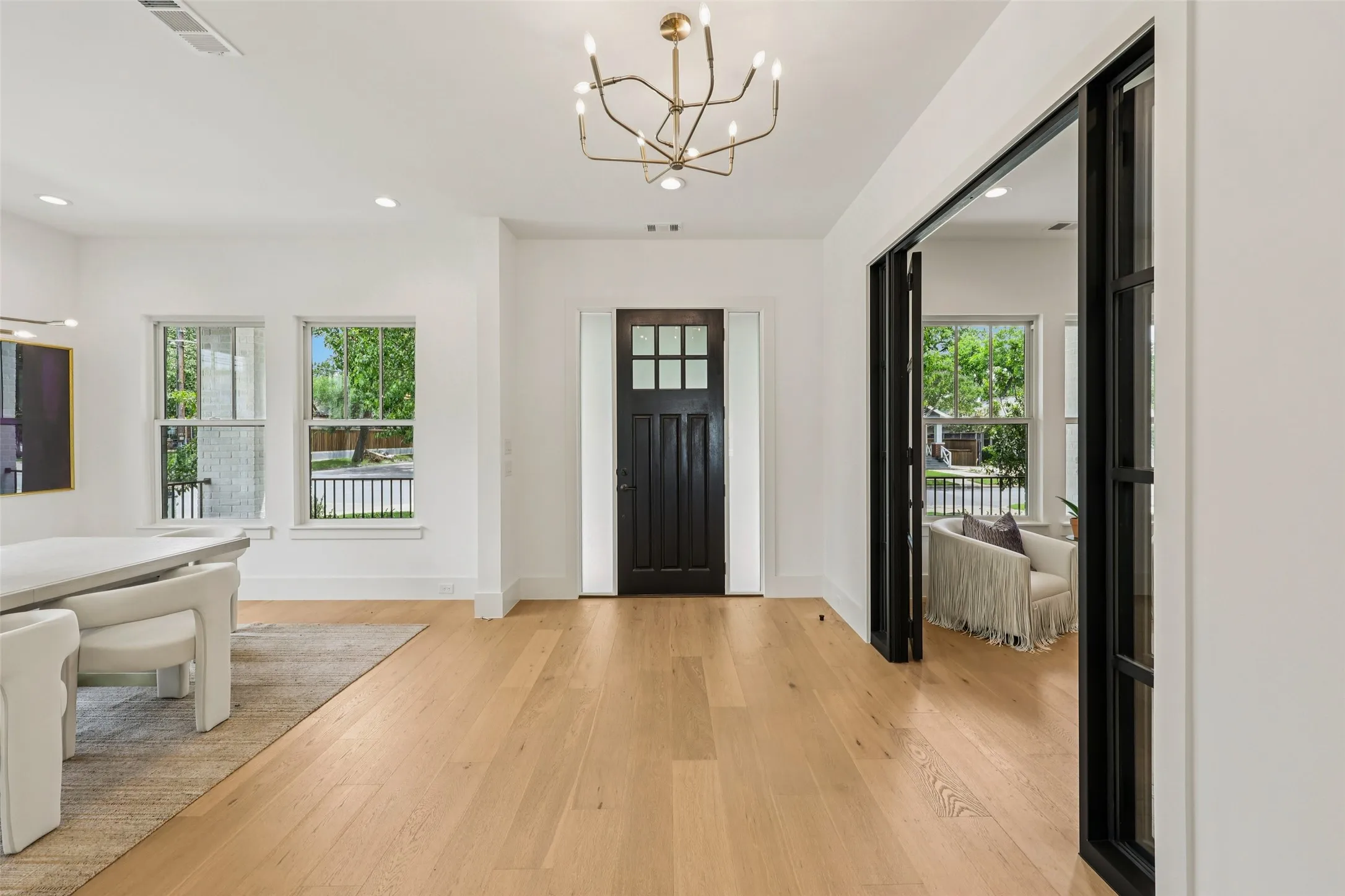 Light wood-finish flooring, a black paneled entry door, modern chandelier, and recessed lighting