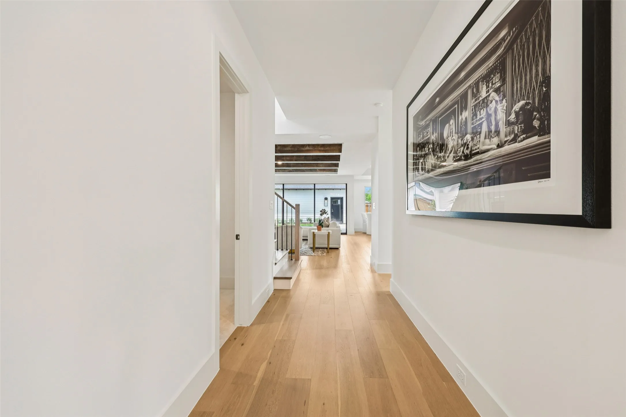 Bright hallway with light wood-finish flooring, white walls, and a partial staircase with dark treads and light risers