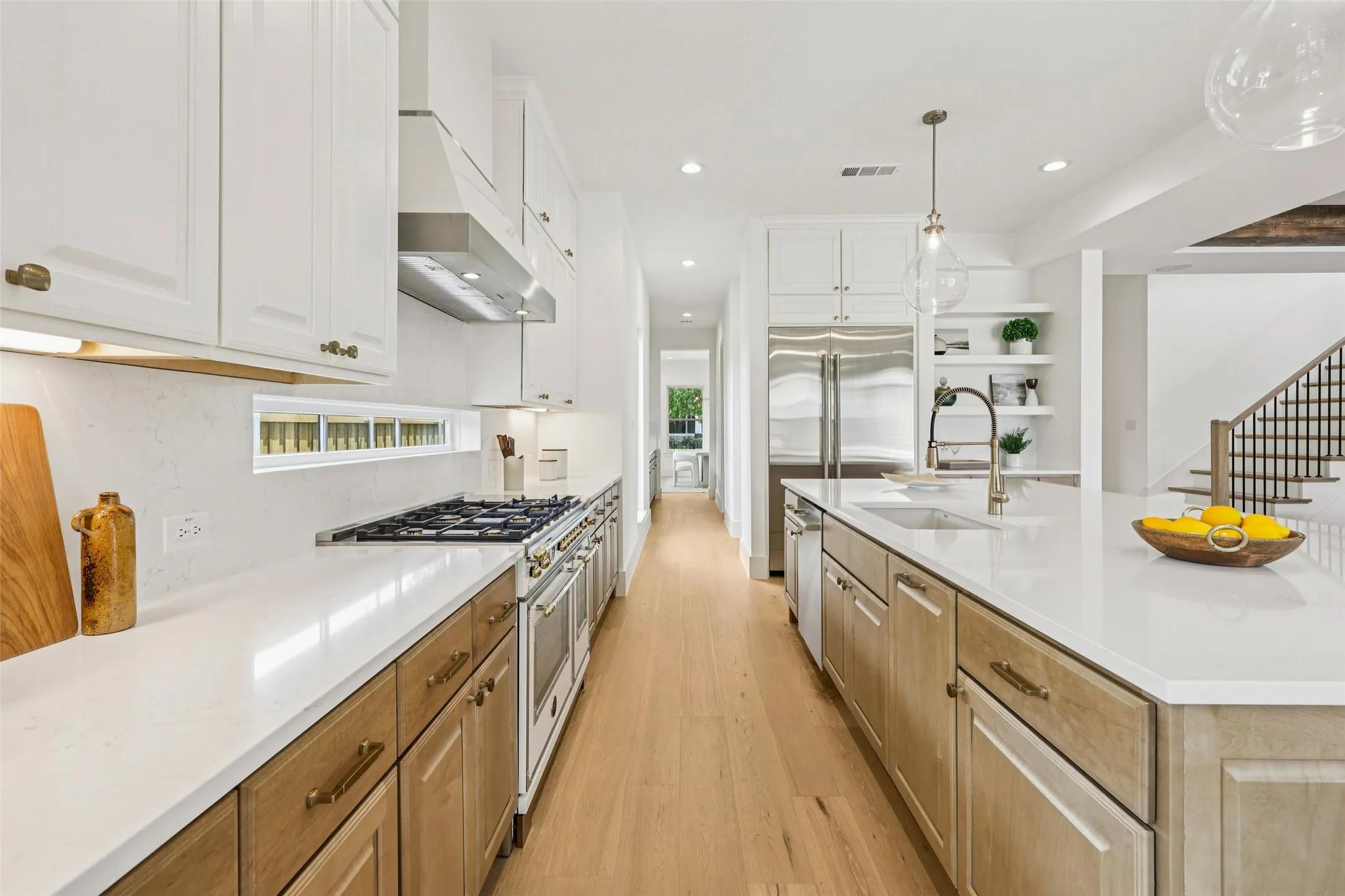 Stainless steel appliances, wood-finish flooring, white cabinetry, integrated range hood, and an oversized kitchen island