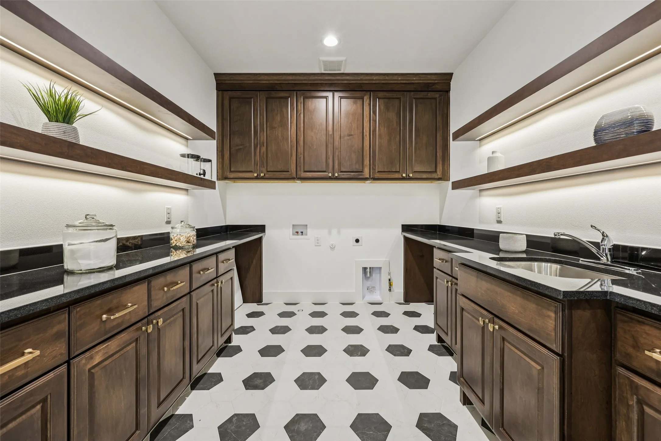 Laundry room featuring dark wood-finish cabinetry, black countertops, a utility sink, open shelving with under-shelf lighting, and hexagonal tile flooring