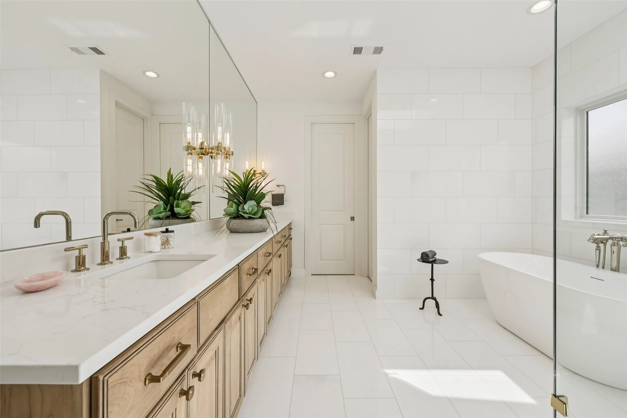 Dual vanity with light wood-finish cabinetry, white countertop with integrated sinks, and brushed gold fixtures