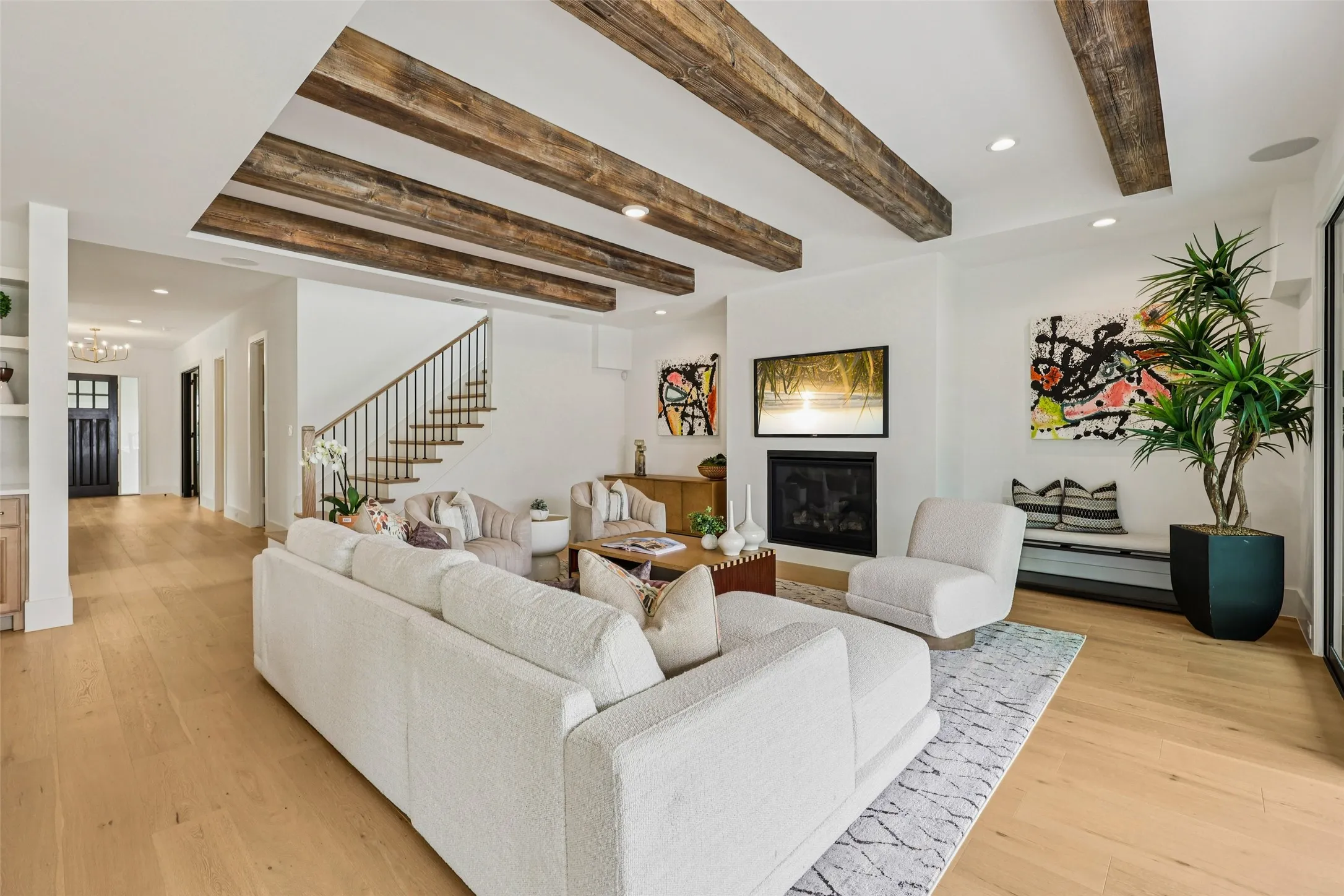 Recessed ceiling with exposed wood beams, a built-in fireplace, light wood-finish flooring, and a staircase with a wrought iron railing