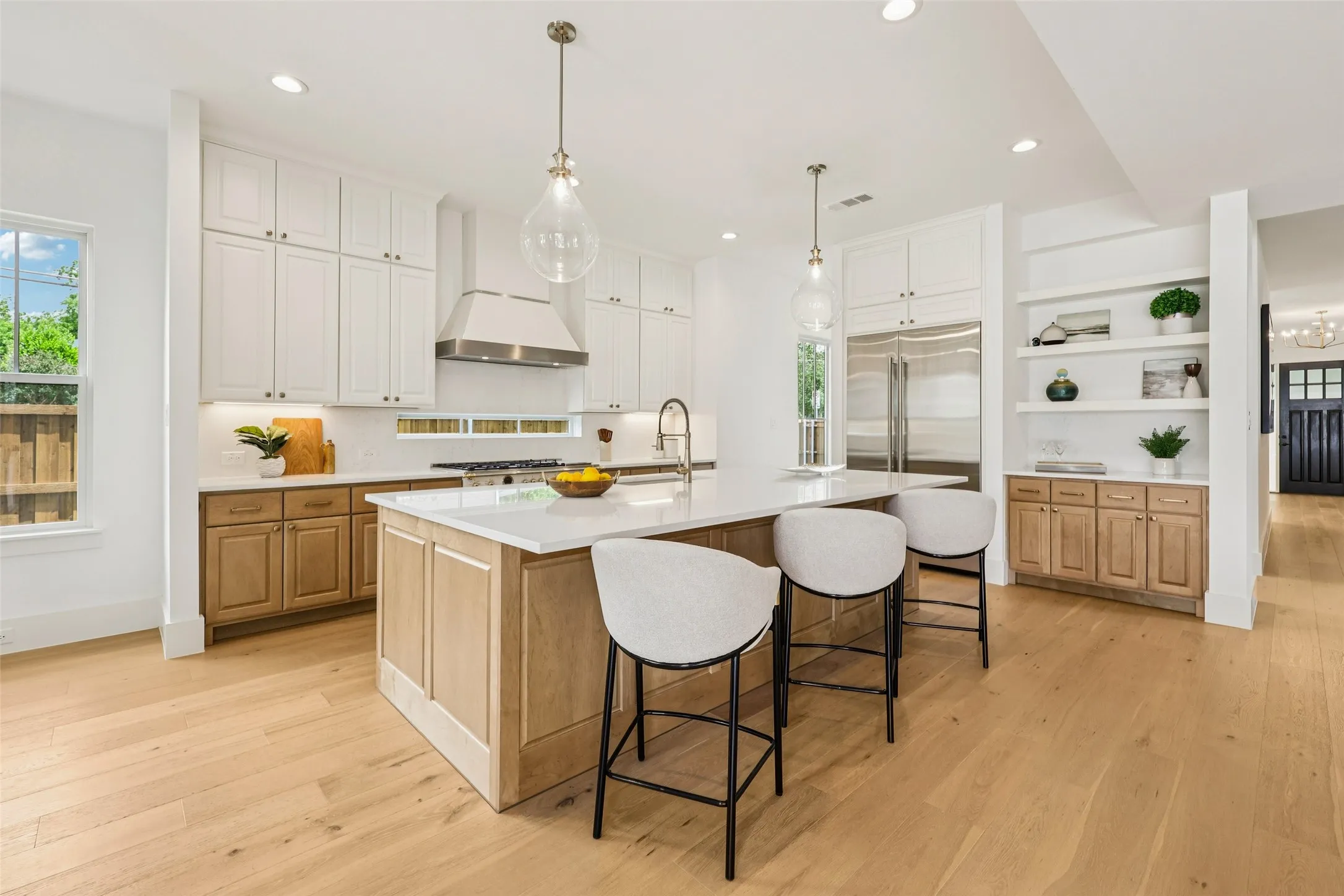 Gourmet kitchen with a large central island, white shaker cabinetry, stainless steel appliances, and wood-finish flooring