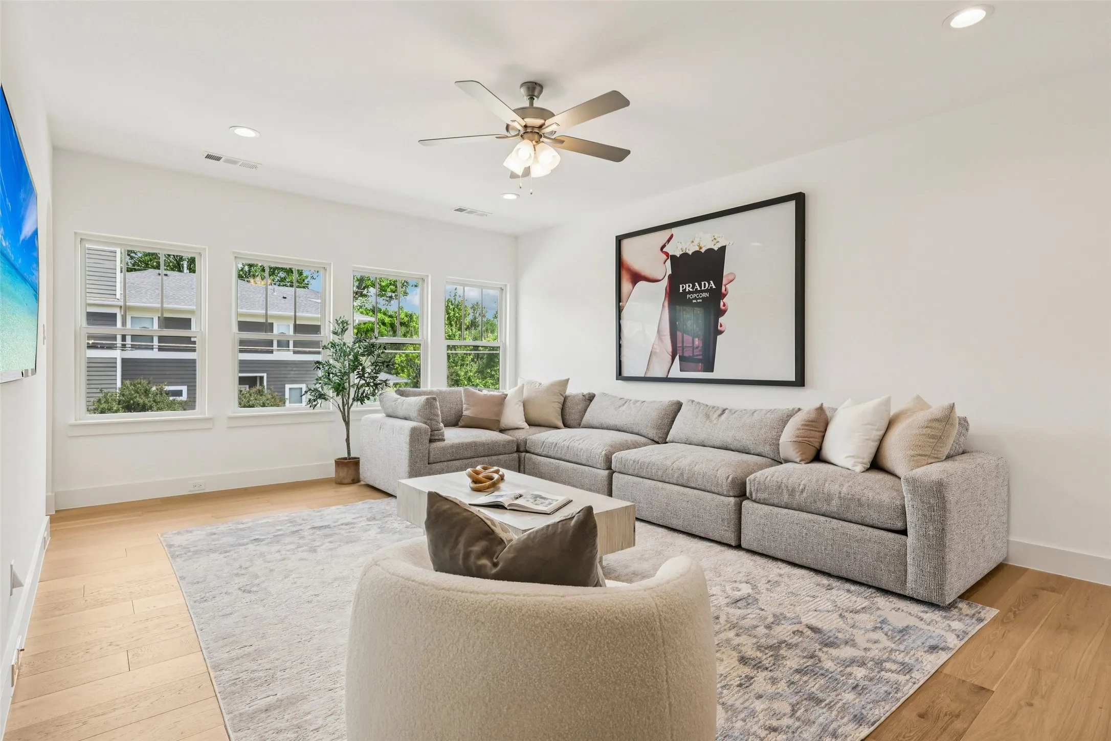 Spacious living area featuring light wood-finish flooring, recessed lighting, a ceiling fan, and multiple large windows