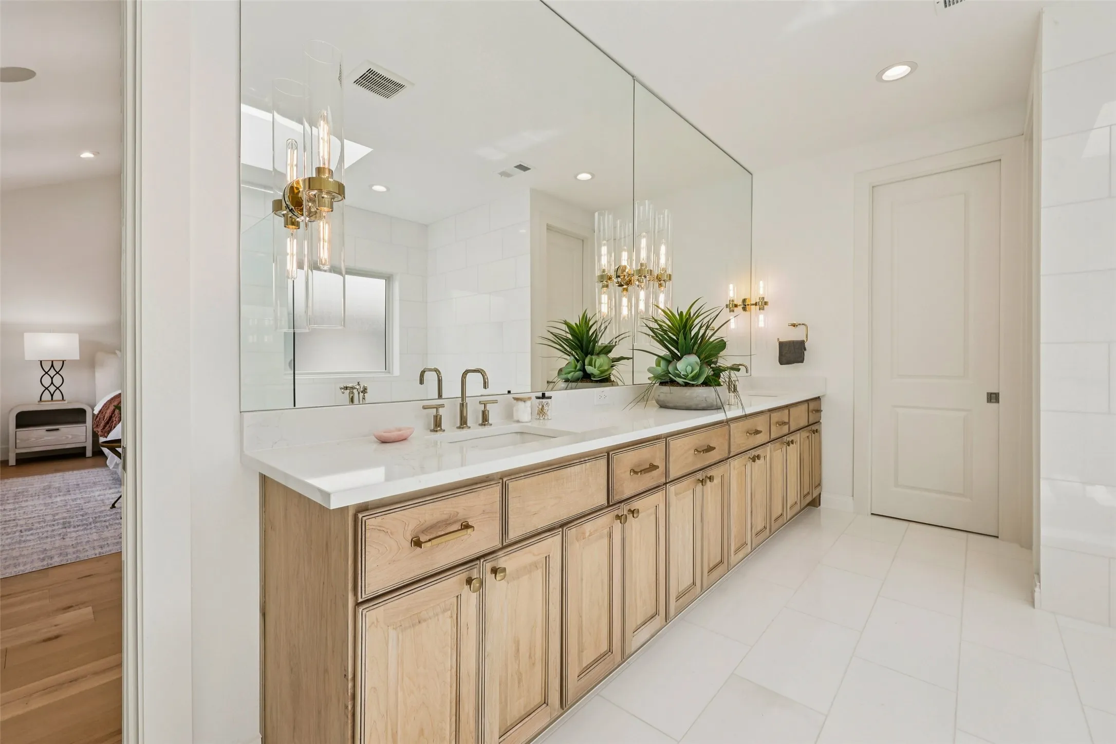 Dual vanity with light wood cabinetry, white countertop, double basin sinks, and brass-tone fixtures