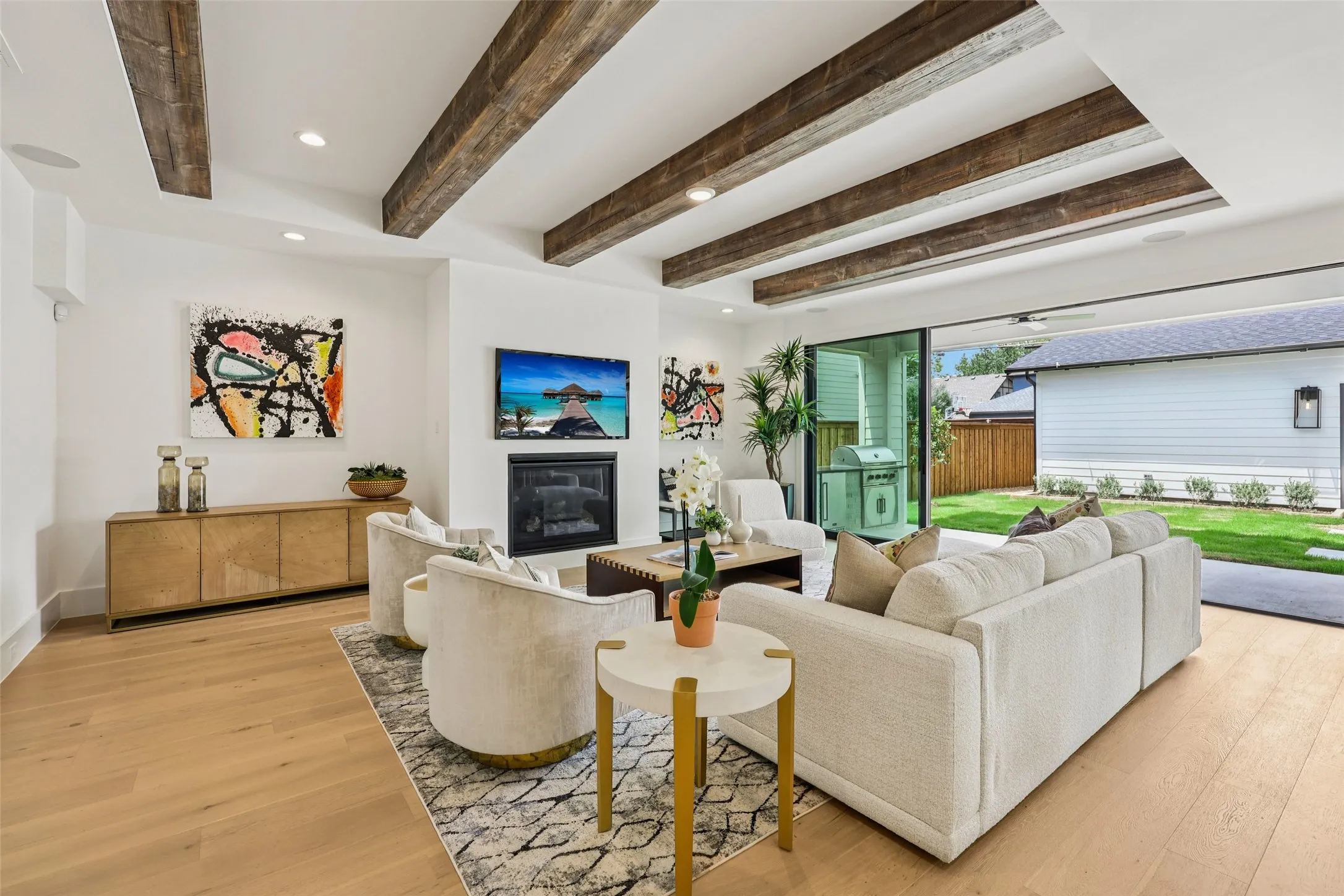 Hardwood flooring, exposed ceiling beams, built-in fireplace, and expansive sliding glass doors opening to a manicured lawn