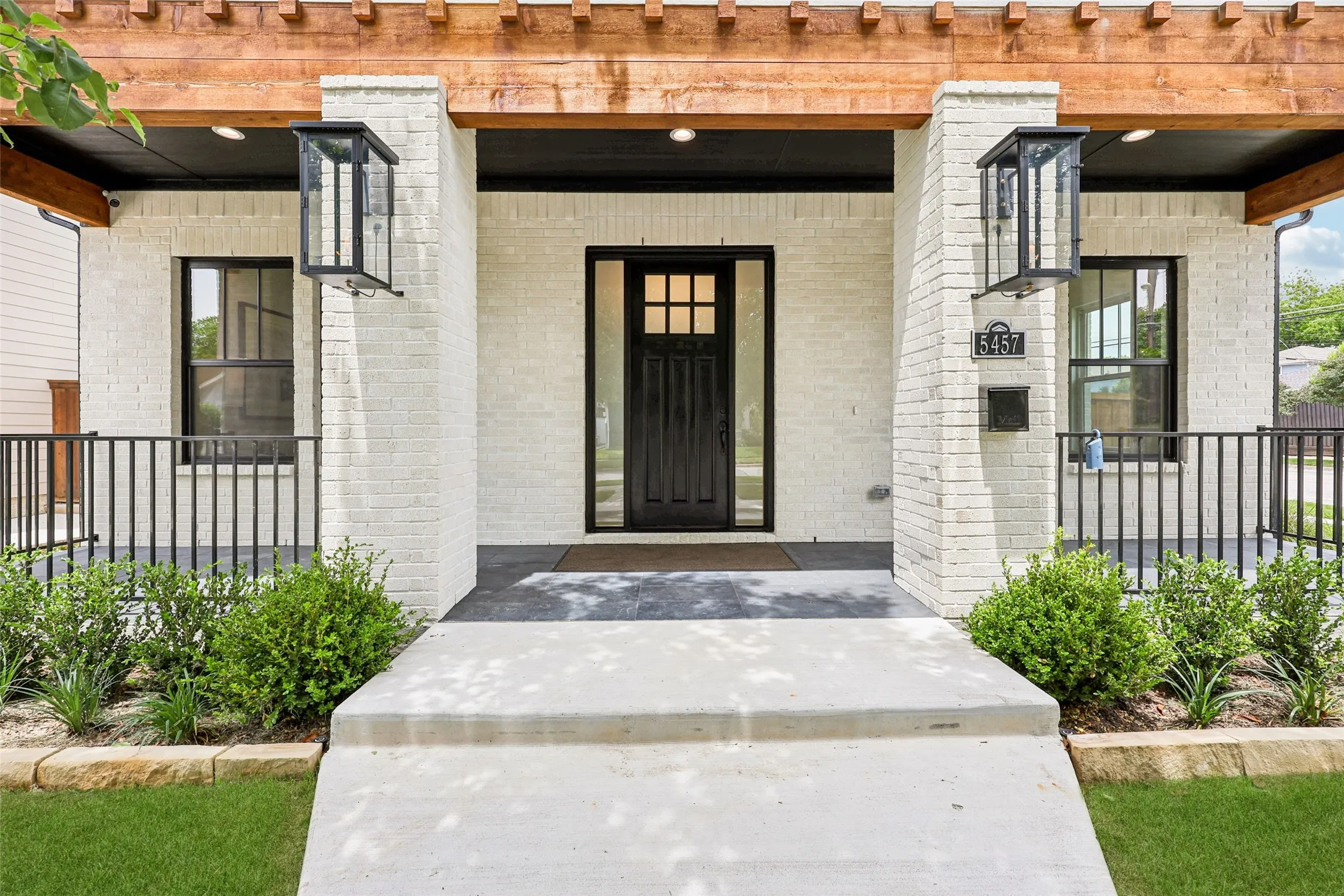 White brick exterior with a black front door, black-framed windows, and a wood pergola