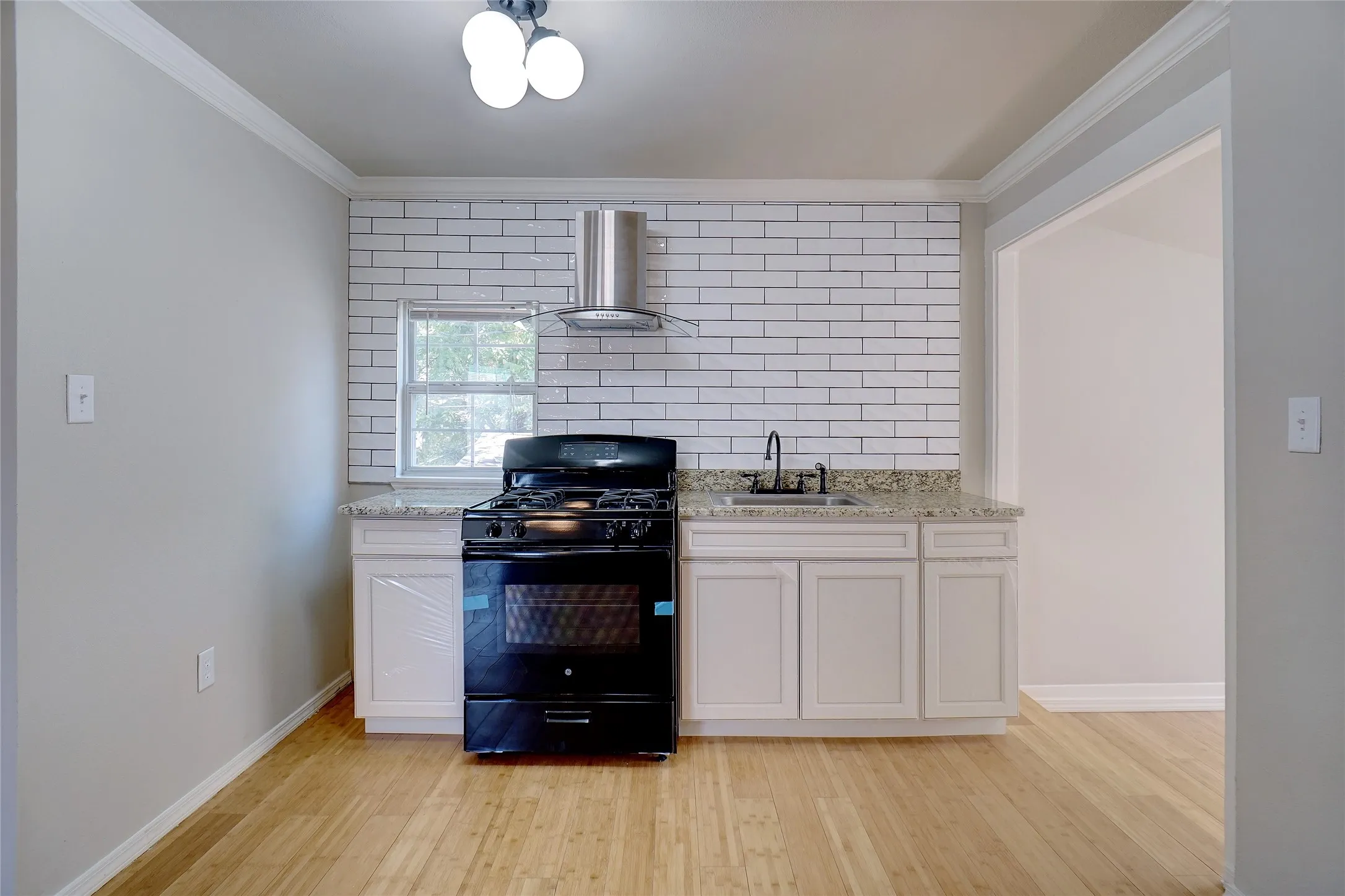 Kitchen featuring light wood-finish flooring, white subway tile backsplash, white cabinetry, a black range with a stainless steel range hood, and granite countertops