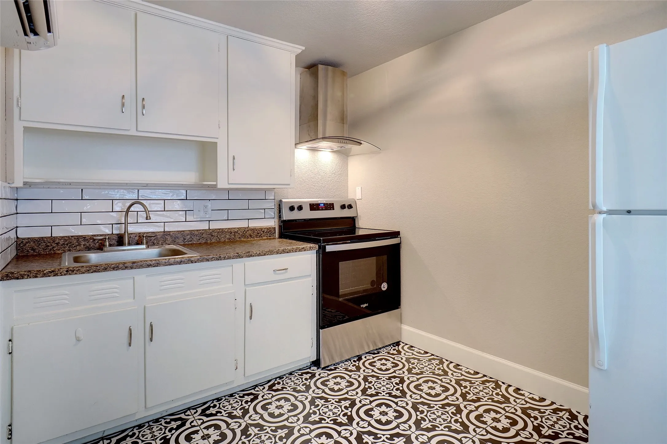 White cabinetry, patterned floor tiling, subway tile backsplash, stainless steel range with hood, and a built-in sink