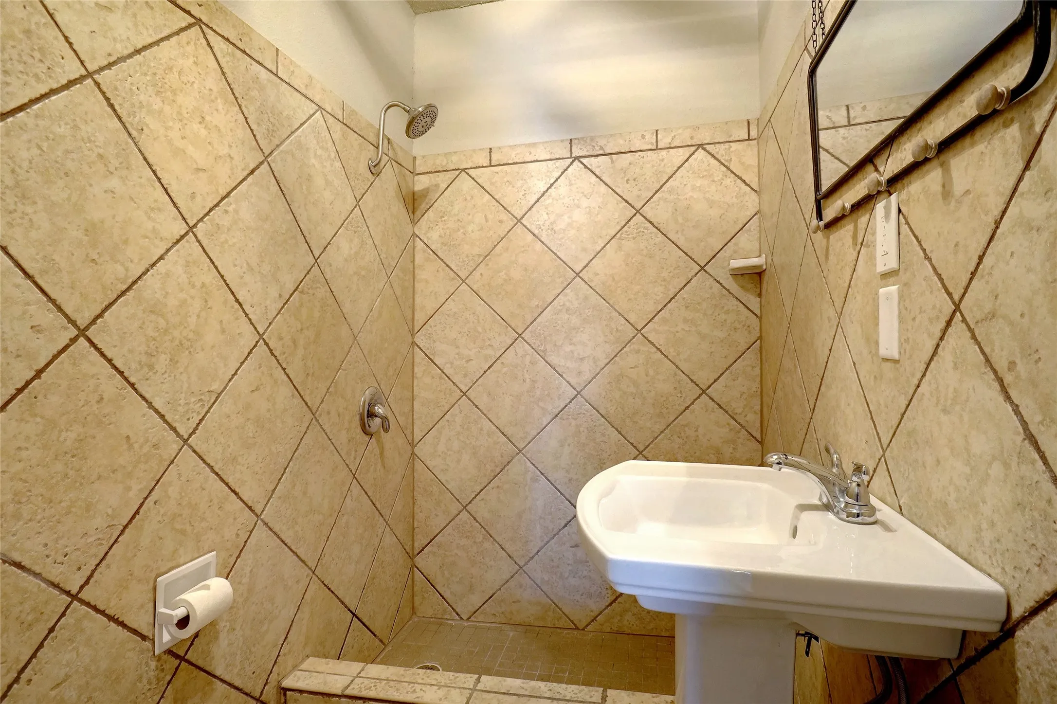 Pedestal sink with chrome faucet, full-height tile shower surround, and a wall-mounted shower head