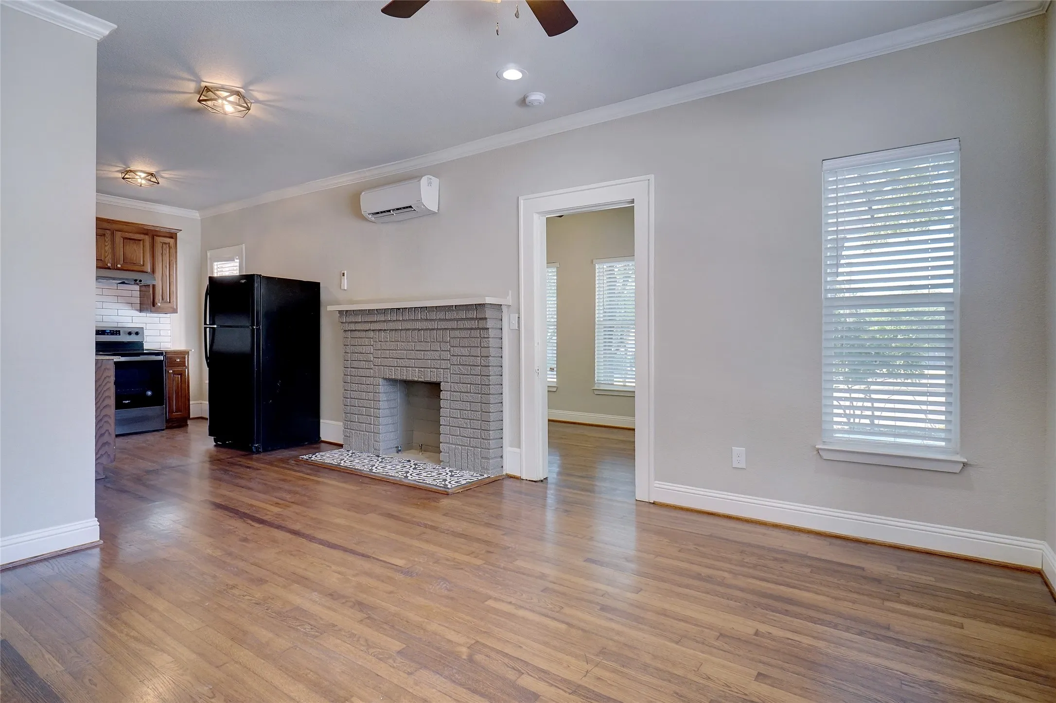 Hardwood flooring throughout, brick fireplace with decorative stone hearth, built-in air conditioning unit, crown molding, and window with blinds