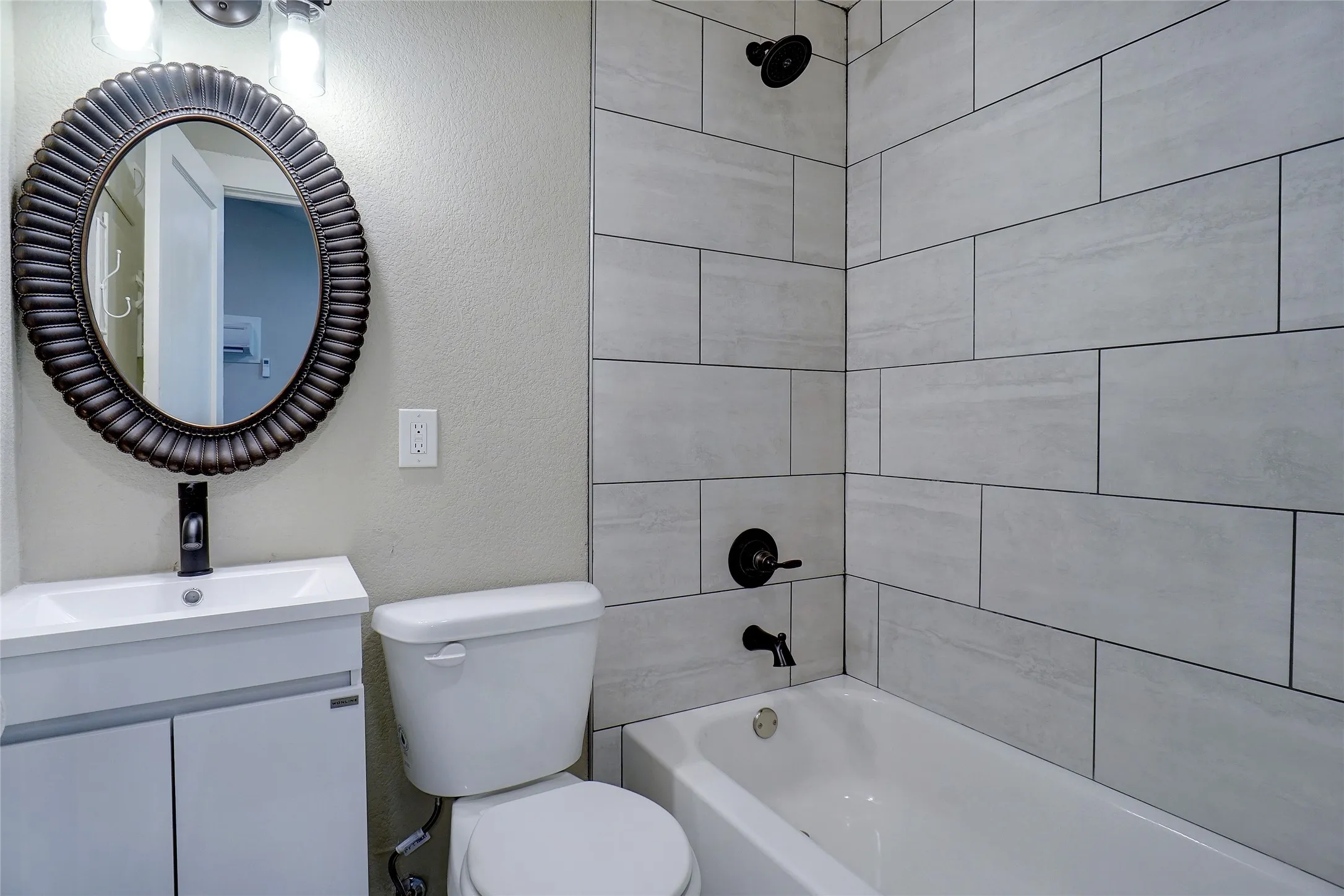 Modern bathroom featuring a white vanity with integrated sink, oil-rubbed bronze fixtures, an oval mirror with a decorative frame, a white toilet, and subway-style tile surrounding the bathtub