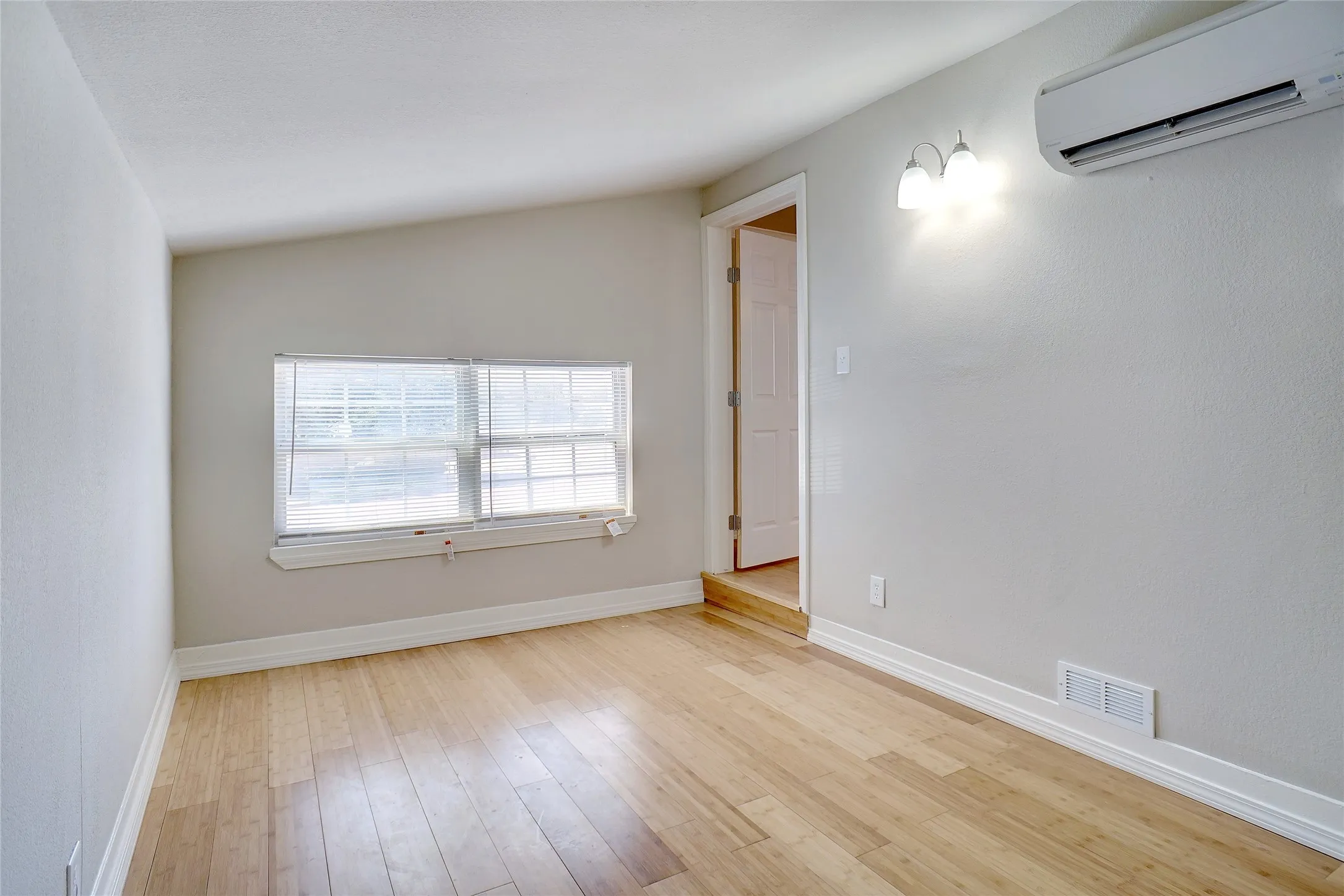 Hardwood-style flooring, white trim, wall-mounted lighting fixture, window with blinds, and mini-split AC unit