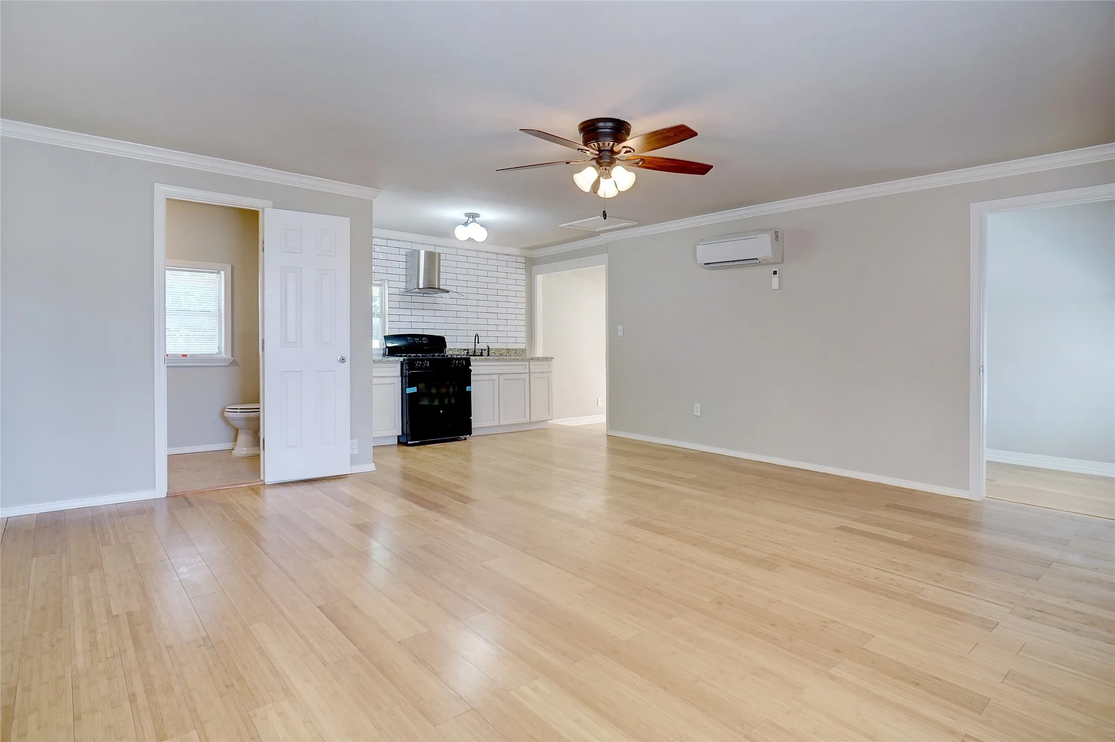 Wood-finish flooring throughout, white cabinetry, dark appliances, stainless steel range hood, and a ceiling fan with integrated lighting