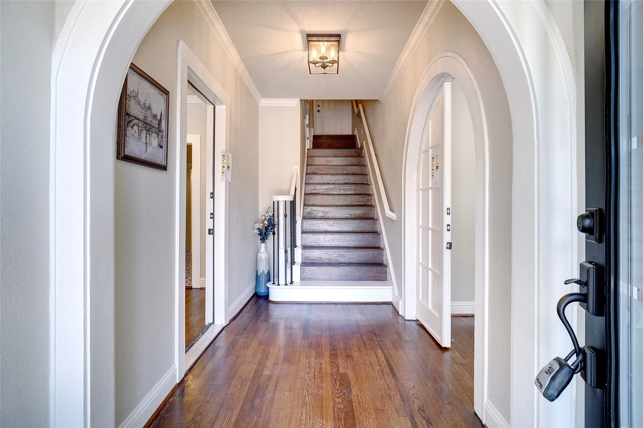 Hardwood flooring, arched doorways, a staircase with white balusters, and a ceiling-mounted light fixture