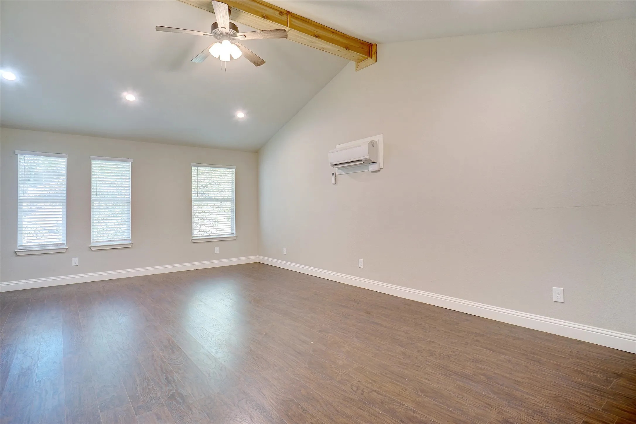 Vaulted ceiling with exposed wood beam, wood-finish flooring, recessed lighting, and wall-mounted climate control unit