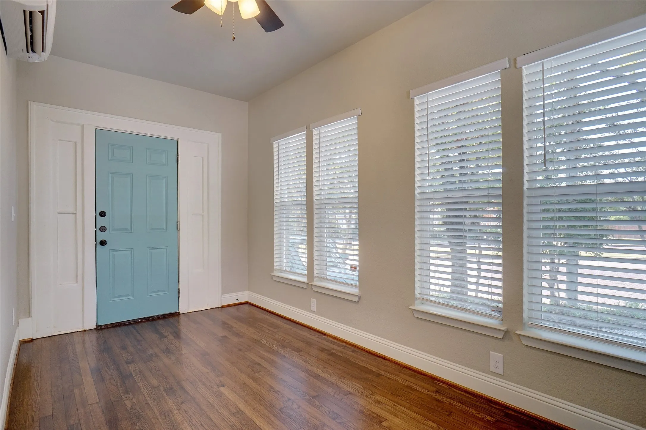 Rich wood-finish flooring, accent door, multiple windows, and a ceiling fan