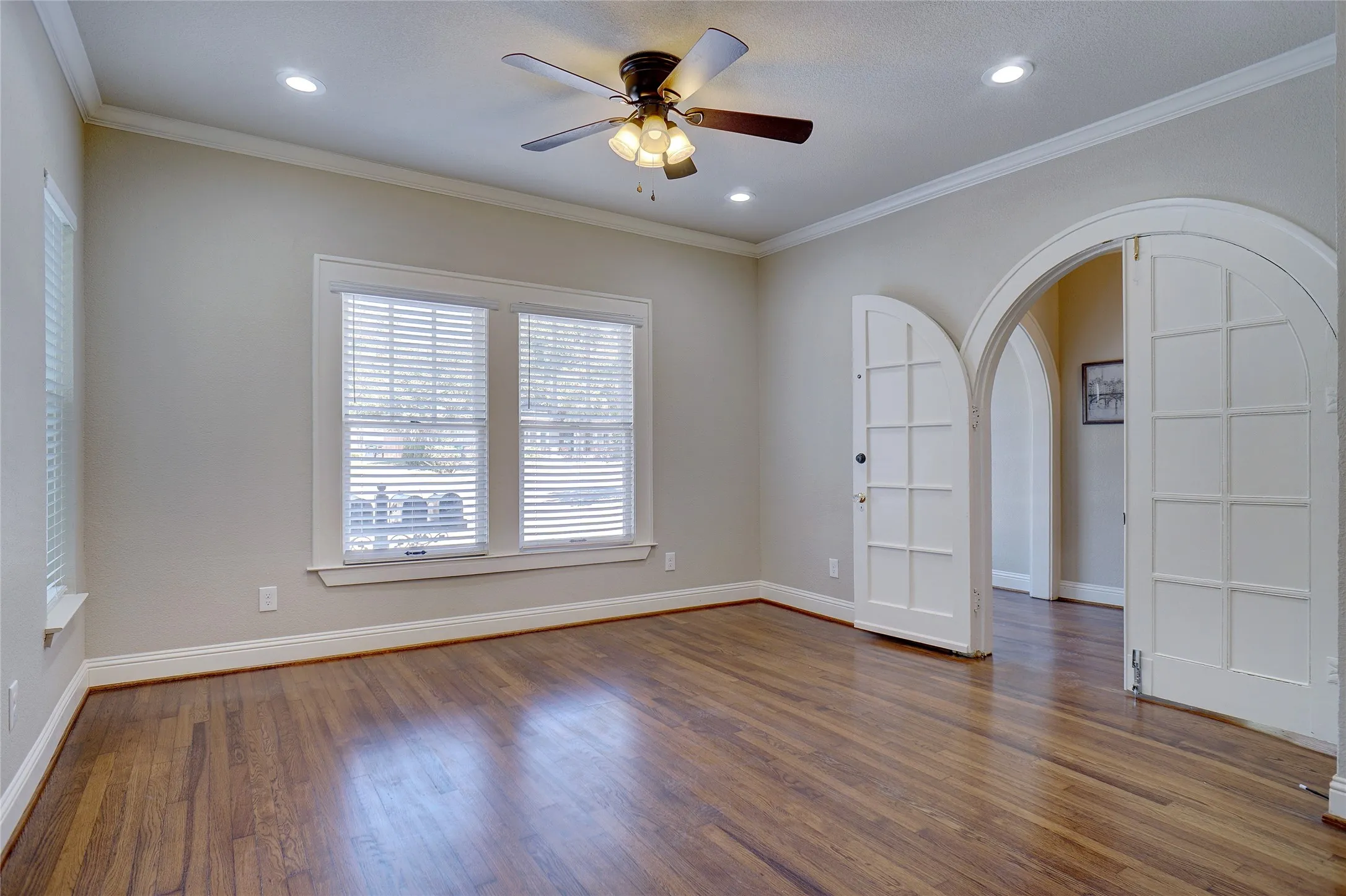 Hardwood flooring, arched doorways, crown molding, recessed lighting, and a ceiling fan