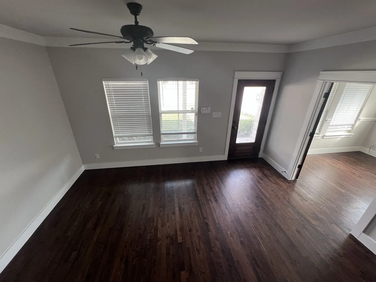 Hardwood flooring, painted interior walls, white window blinds, ceiling fan with light fixture, and a glass-paneled door