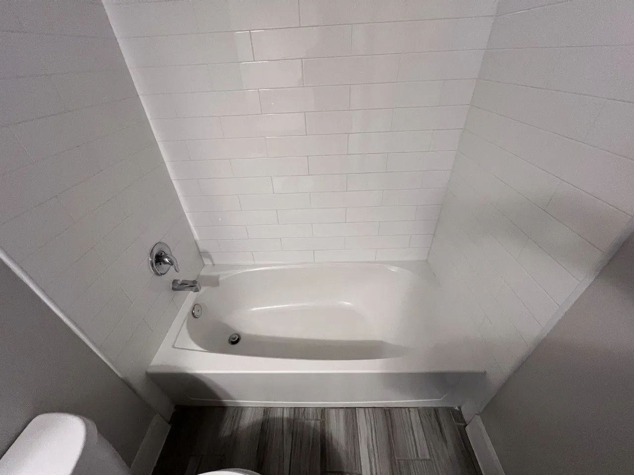 White subway tile surround, polished chrome fixtures, integrated bathtub, and wood-finish flooring