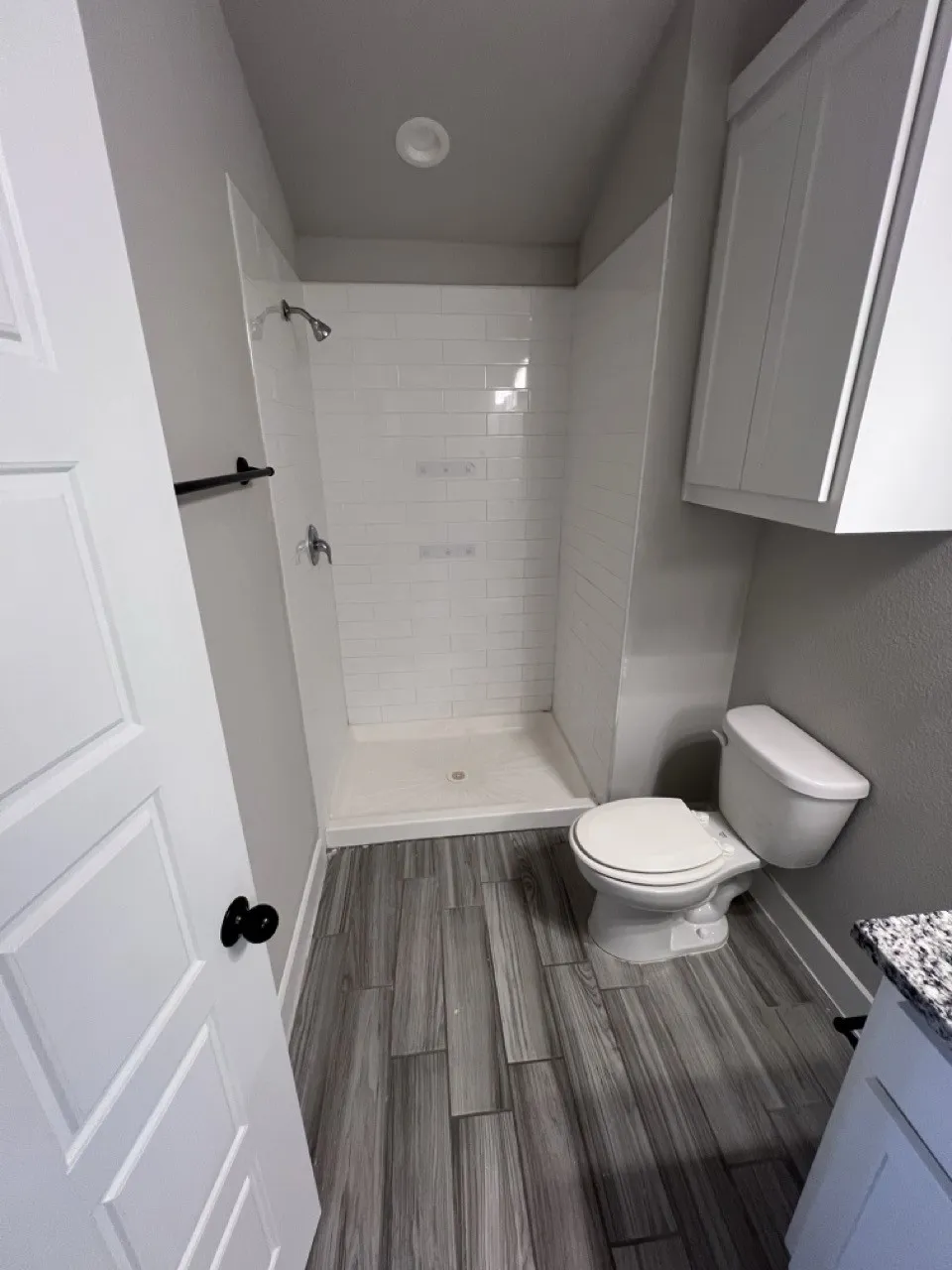 Walk-in shower with white subway tile surround, wood-finish flooring, white wall-mounted cabinetry, recessed lighting, and a granite-look vanity countertop