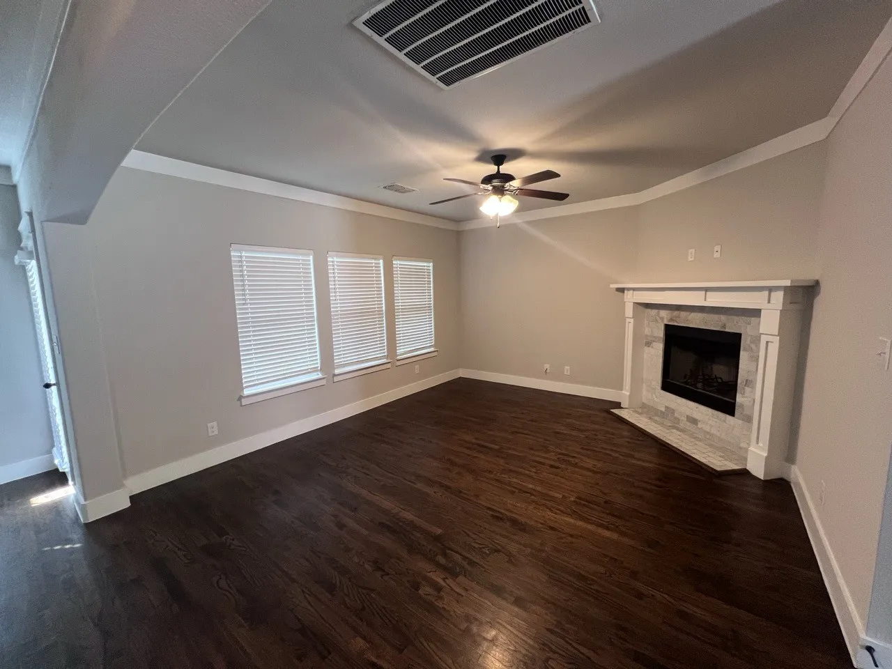 Hardwood flooring, fireplace with stone surround, ceiling fan, crown molding, and multiple windows with blinds
