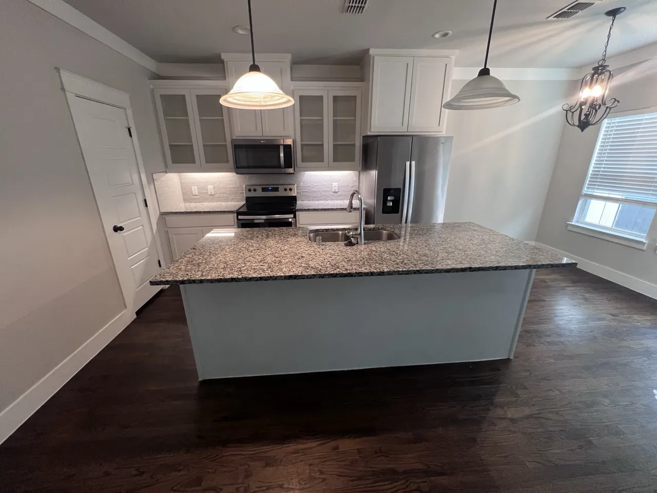 Kitchen featuring an island with stone countertop, stainless steel appliances, white cabinetry, and wood-finish flooring