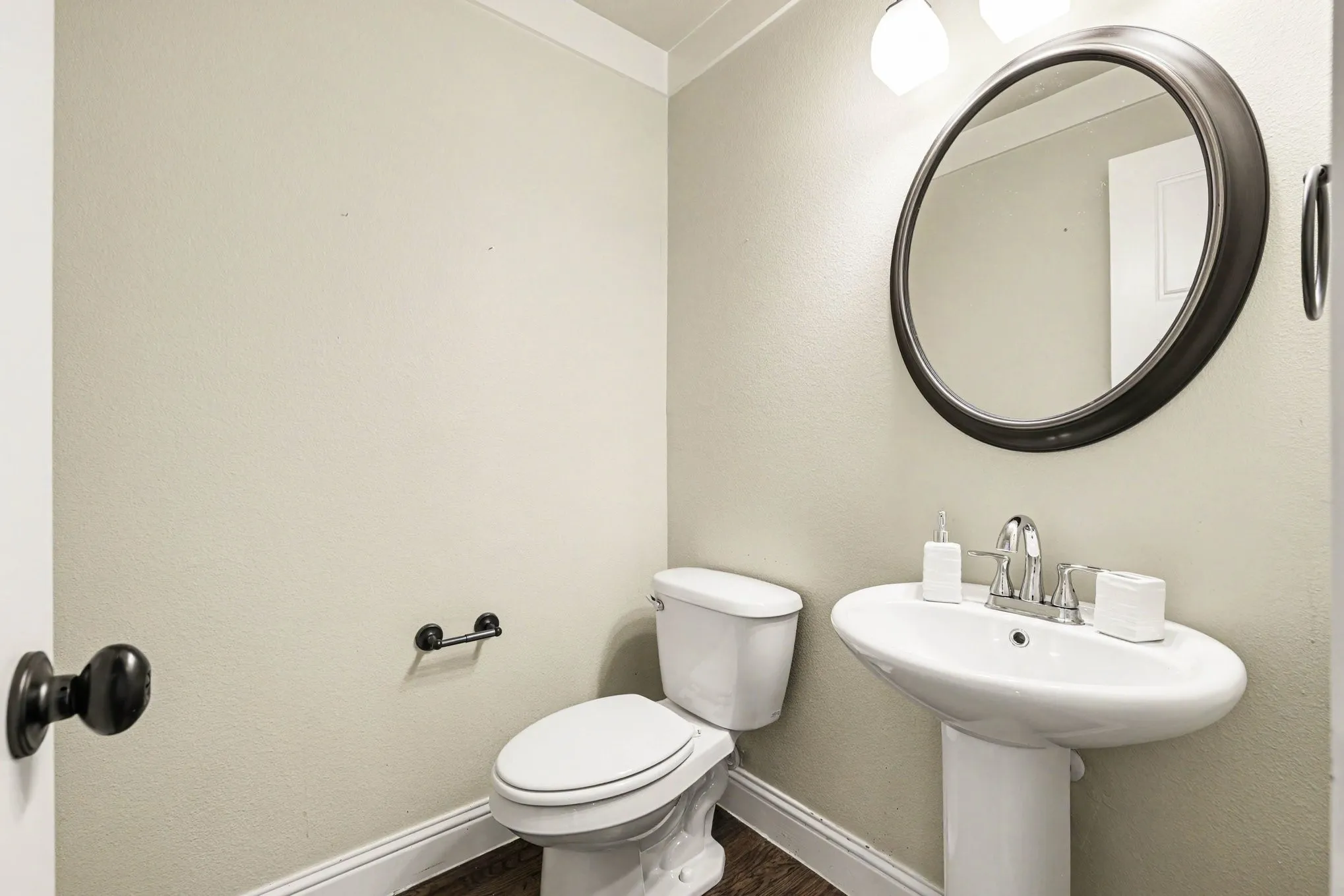 Pedestal sink with chrome faucet, circular framed mirror, and two-light vanity fixture