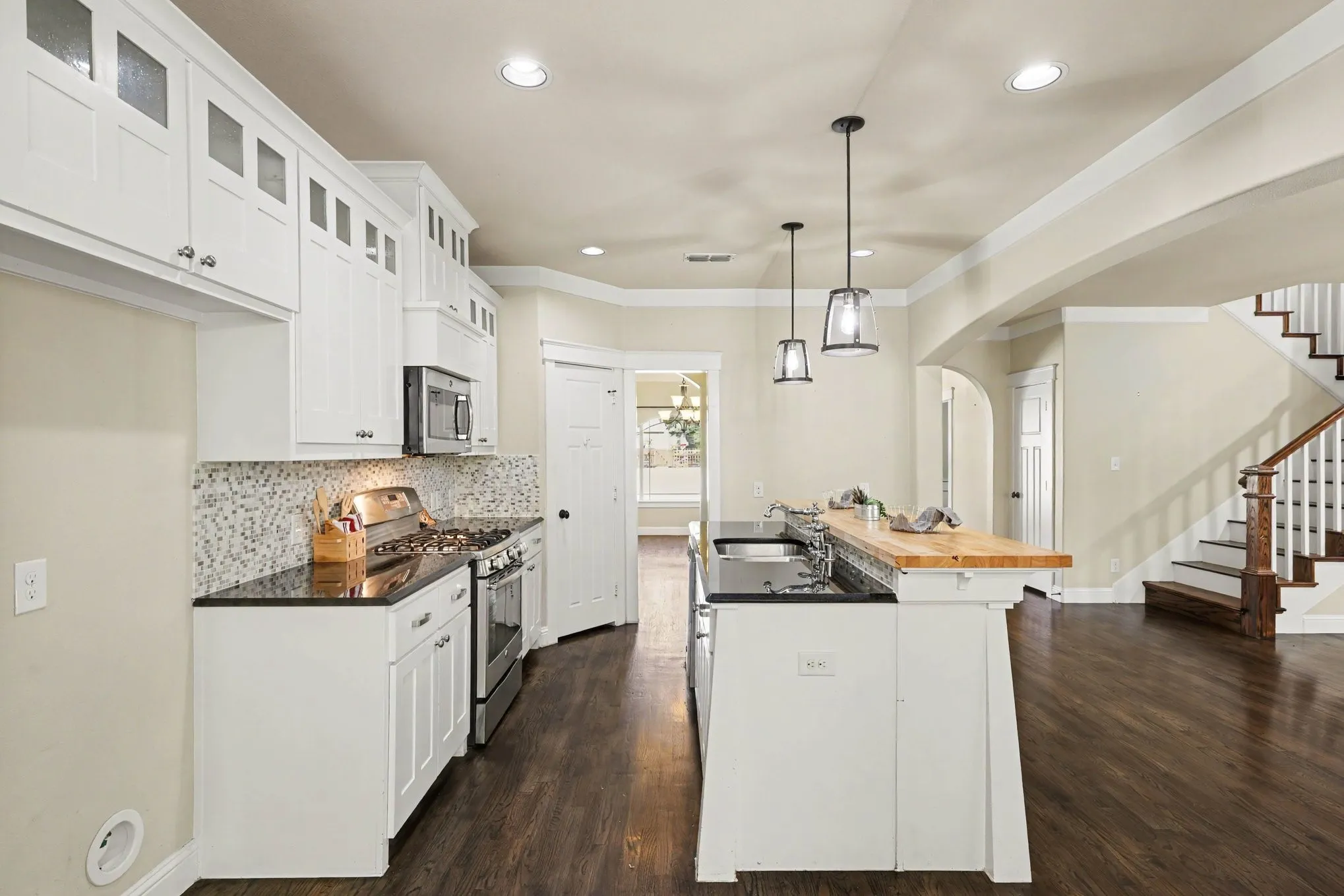 Kitchen featuring white cabinetry with upper glass-front accents, dark countertops, a mosaic tile backsplash, and stainless steel appliances