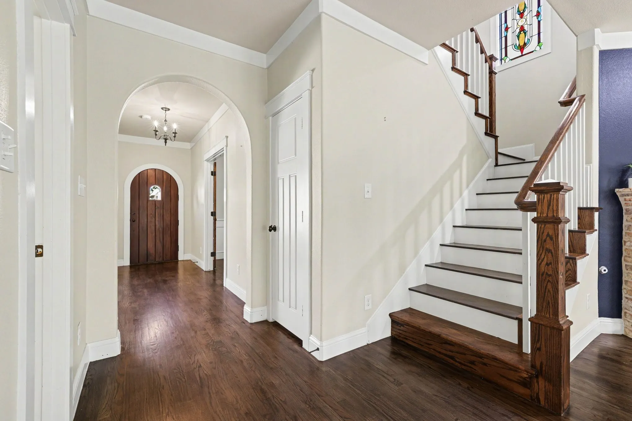 Wood-finish flooring throughout, arched entryway, staircase with wood handrail, classic white trim, and a decorative stained glass window