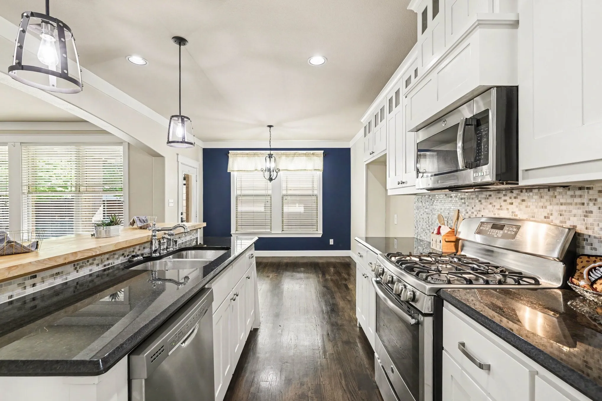 White cabinetry with black countertops, stainless steel appliances, and wood-finish flooring