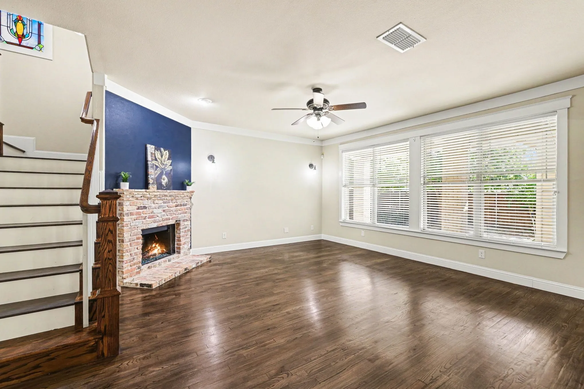 Spacious living area featuring wood-finish flooring, a brick-surround fireplace, and a ceiling fan