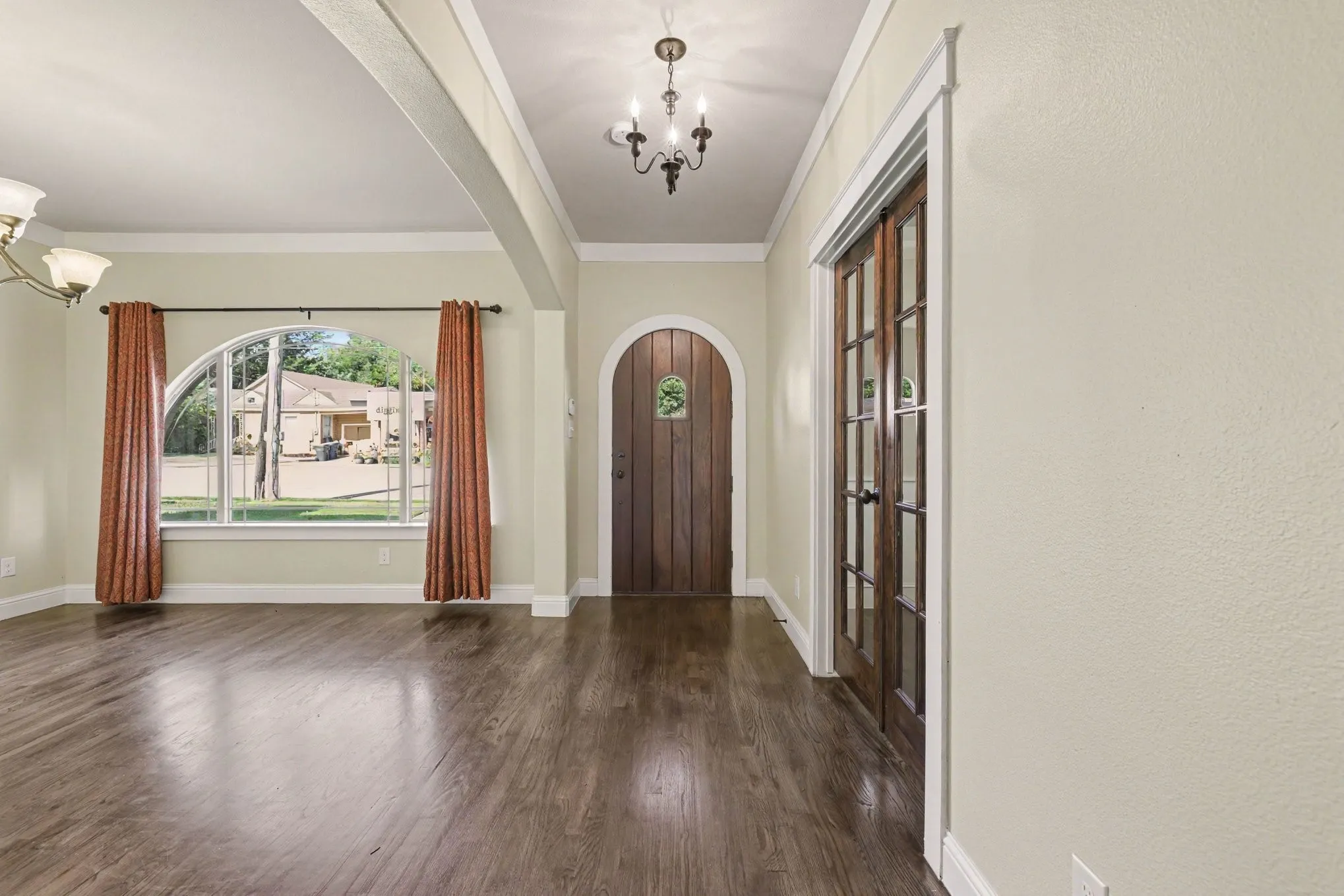 Wood-finish flooring throughout, arched entryway, and dark wood French doors
