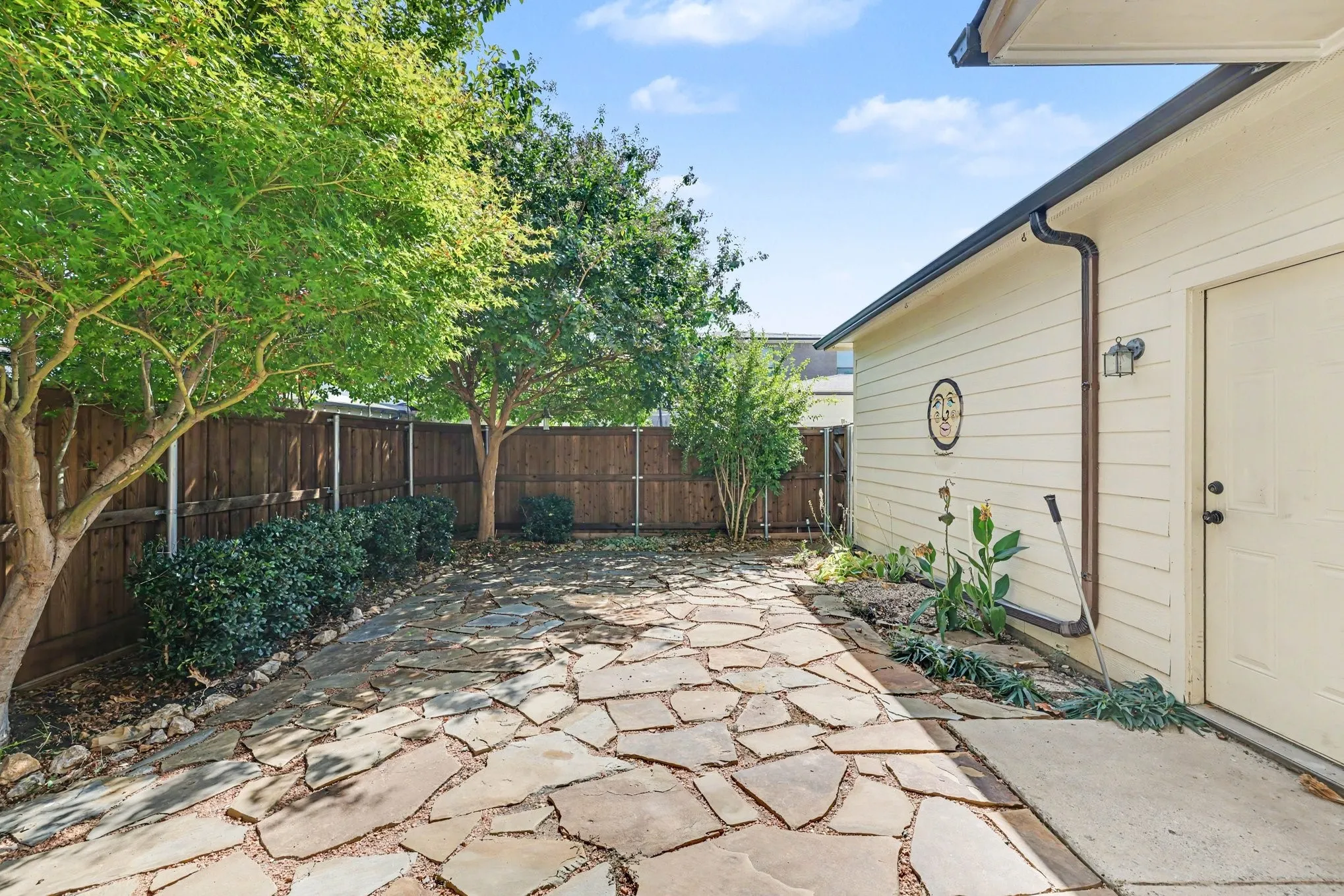 Private outdoor space featuring flagstone paving, mature trees, and a wood privacy fence