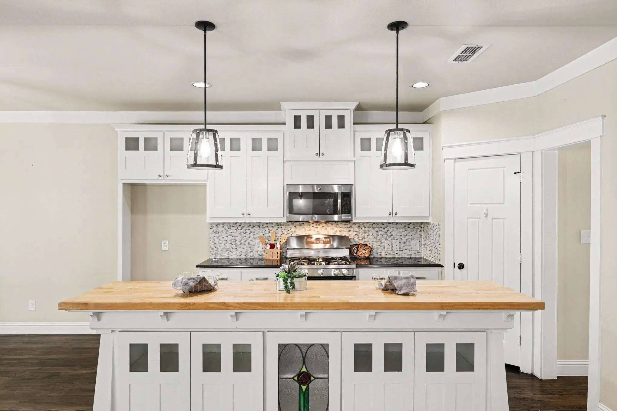 Kitchen island with wood-finish countertop, white cabinetry with clear glass inserts, stainless steel appliances, and a mosaic tile backsplash