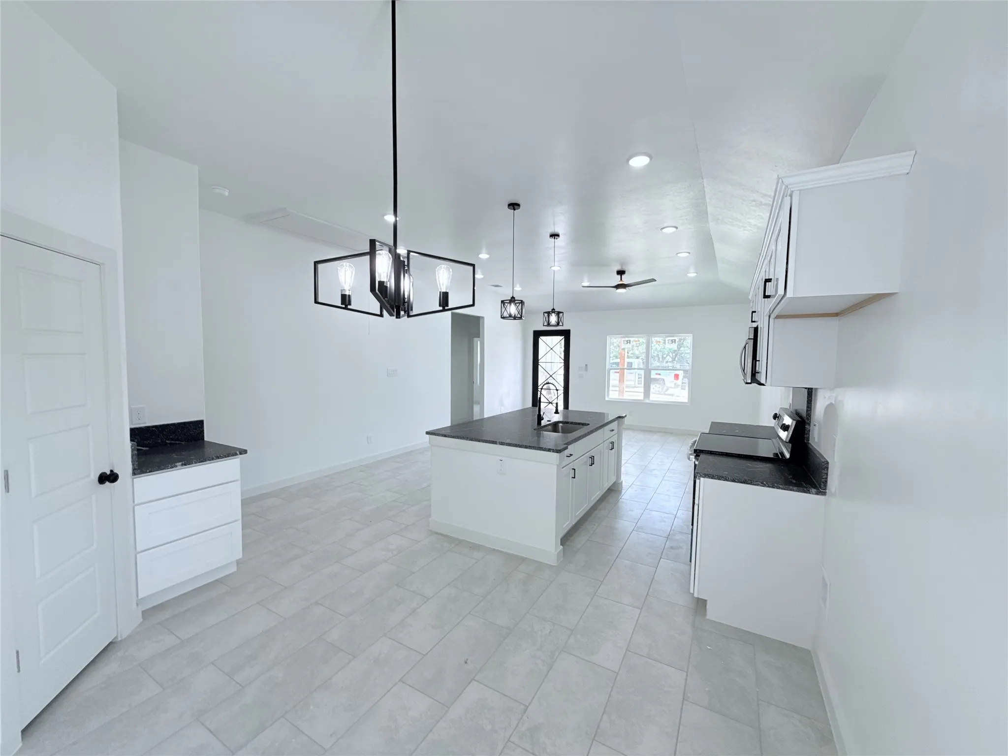 Spacious kitchen featuring an island with a sink, white cabinetry, dark stone countertops, and recessed lighting