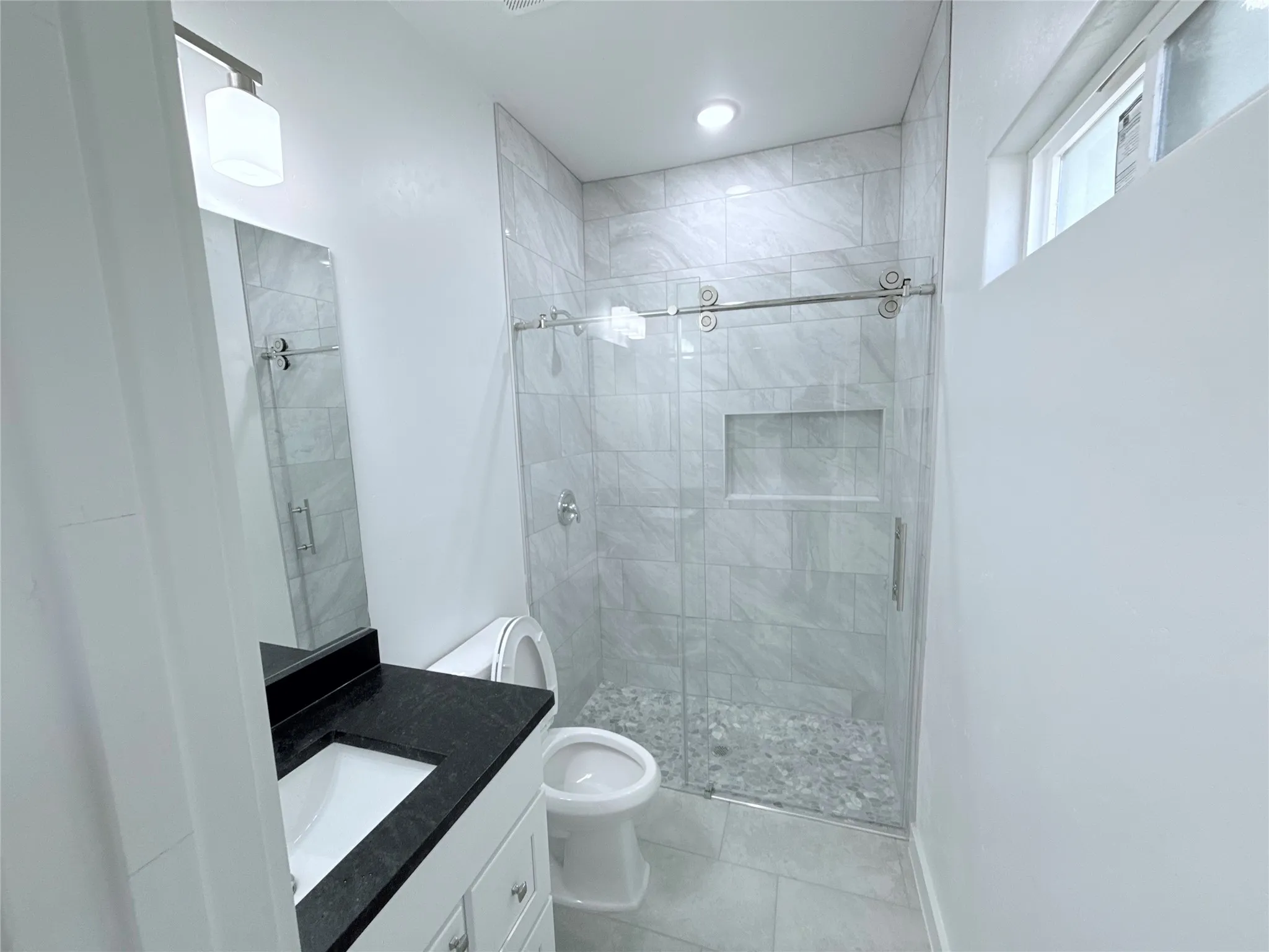 White vanity with dark countertop, large mirror, and glass-enclosed shower with tiled walls and river rock flooring