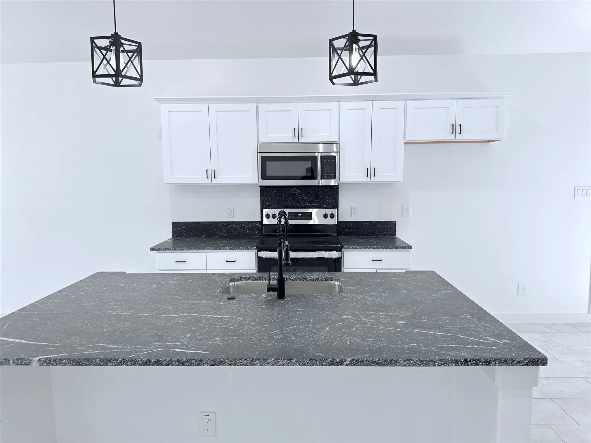 Kitchen featuring shaker-style cabinetry, dark stone countertops, stainless steel appliances, and a kitchen island with an undermount sink