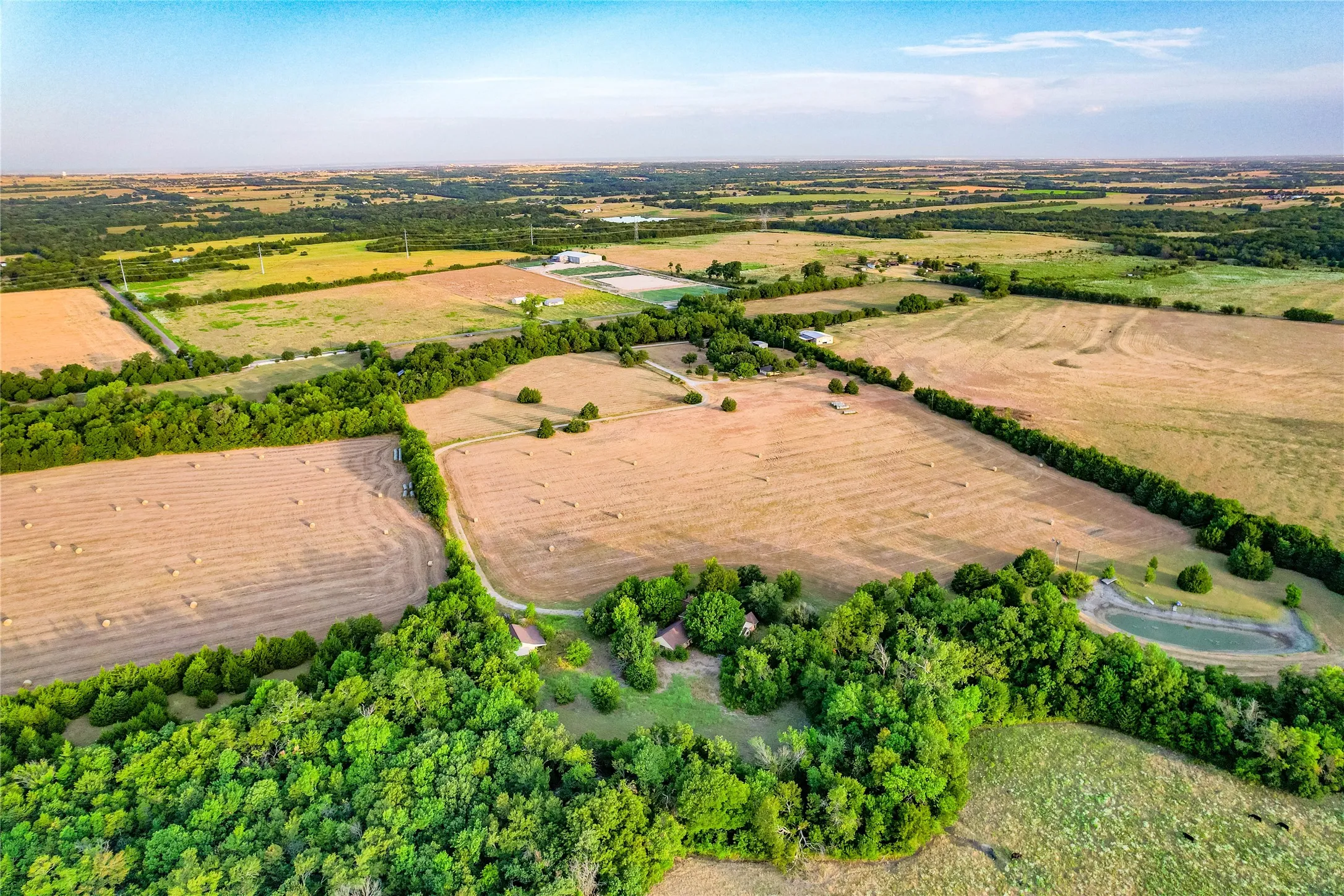 Expansive agricultural land featuring multiple fields, mature tree lines, and a visible pond
