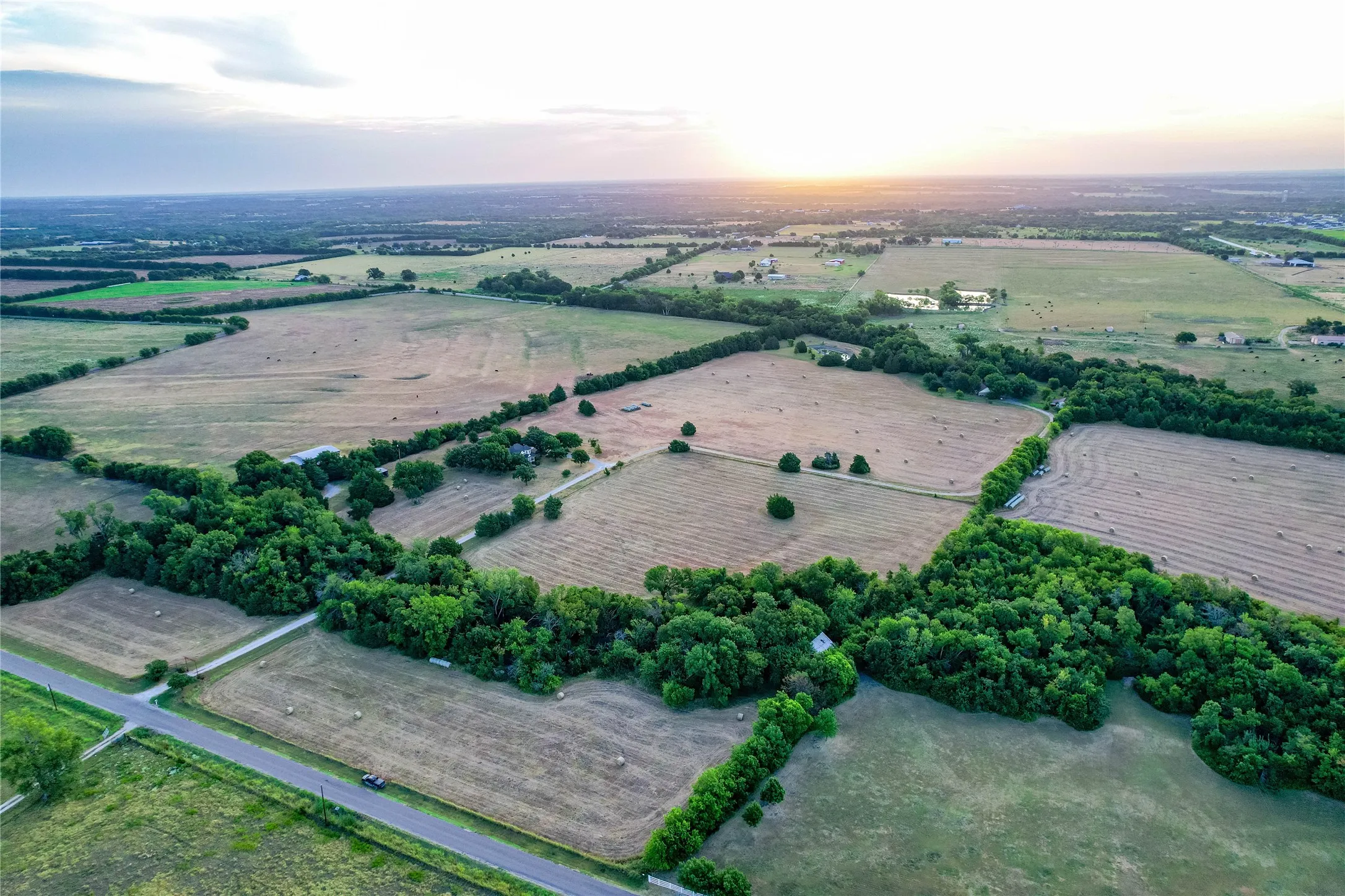 Expansive rural landscape featuring wooded areas, open fields, and a paved road