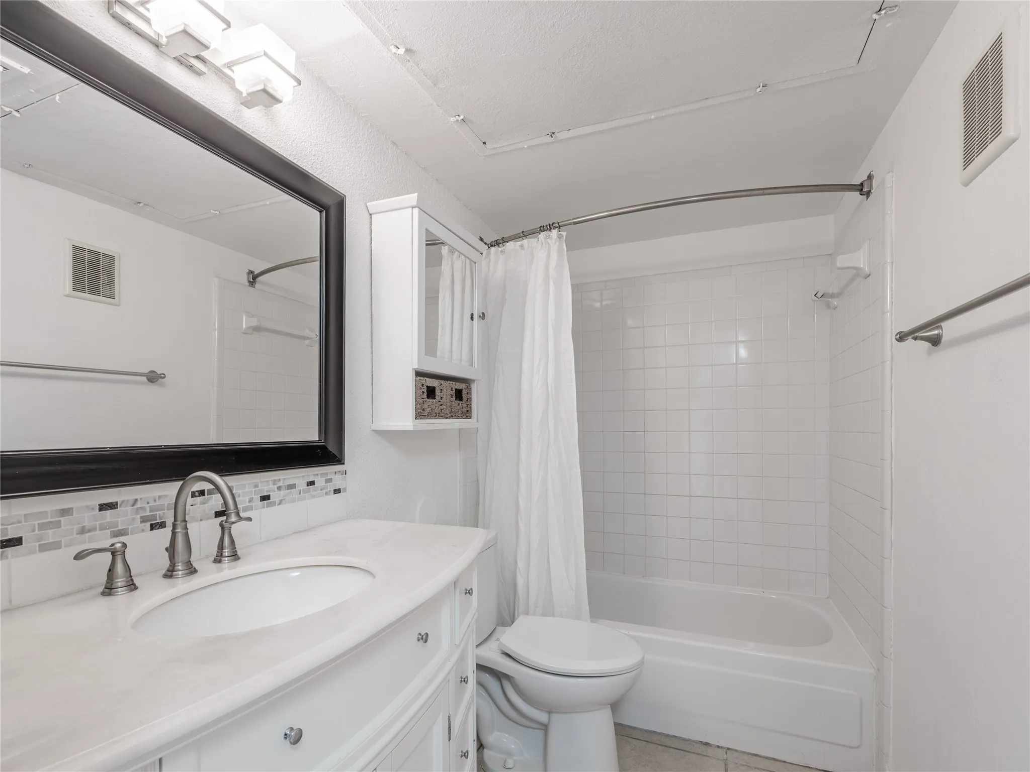 White vanity with an undermount sink, brushed nickel faucet, and a tiled backsplash