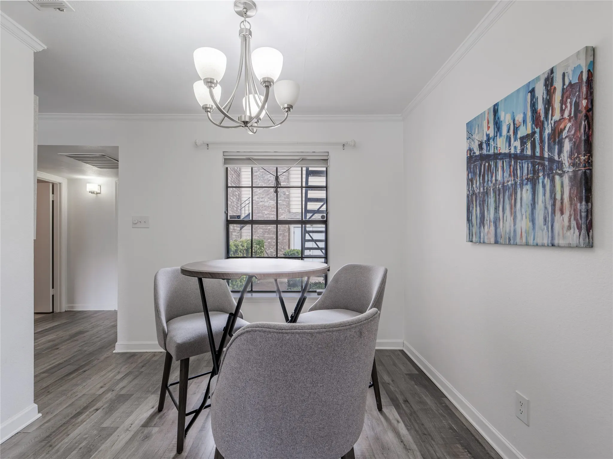 Ceiling-mounted chandelier with frosted glass shades, crown molding, wood-finish flooring, and a fixed window with divided lites