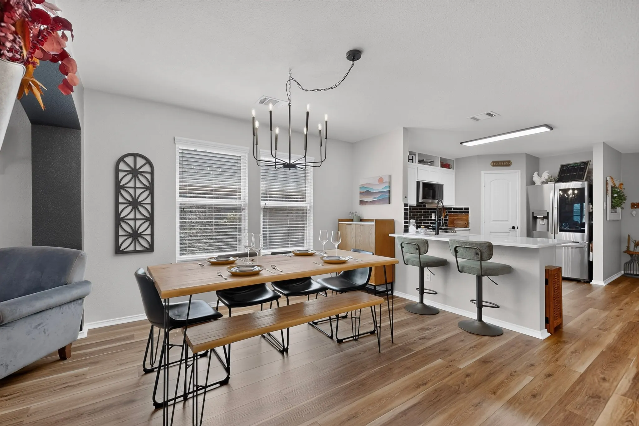 Wood-finish flooring throughout, kitchen with white cabinetry, black subway tile backsplash, and an island with bar seating