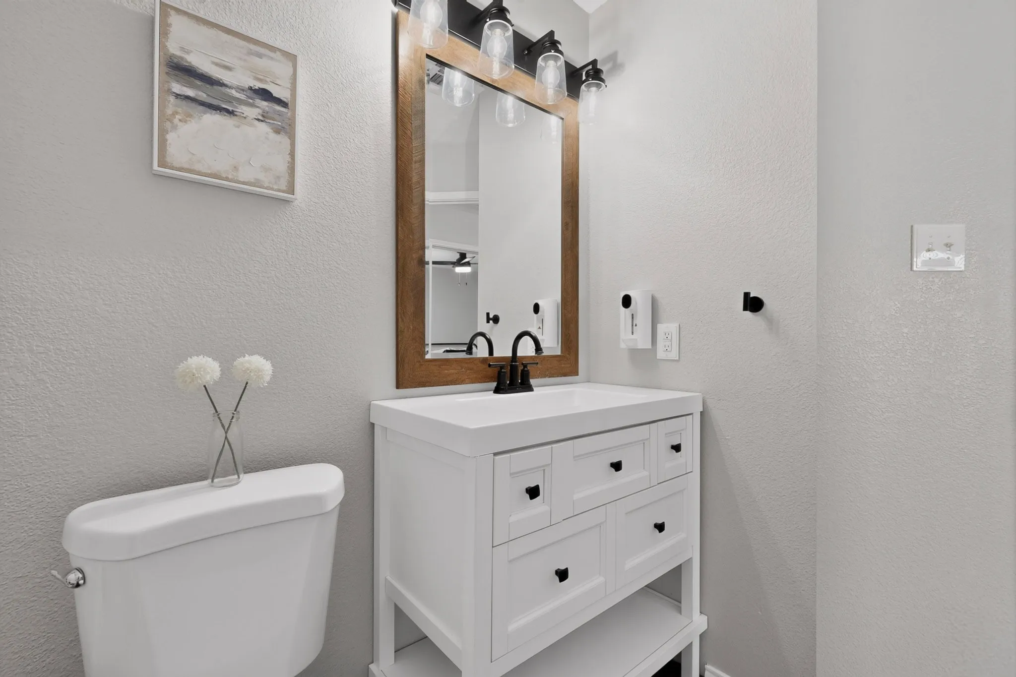 White single vanity with integrated sink, wood-framed mirror, and black wall-mounted faucet