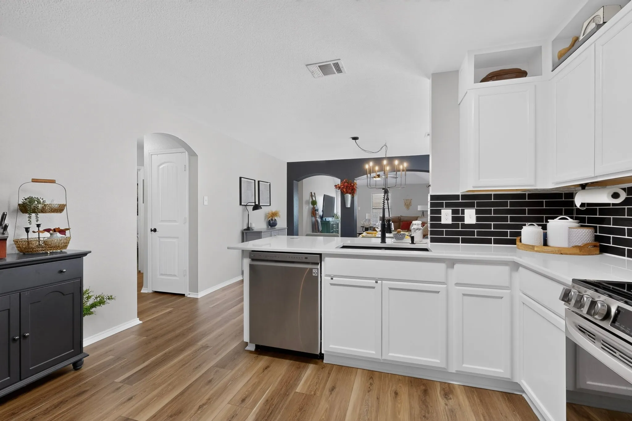 White cabinetry, black subway tile backsplash, stainless steel appliances, wood-finish flooring, and an arched doorway