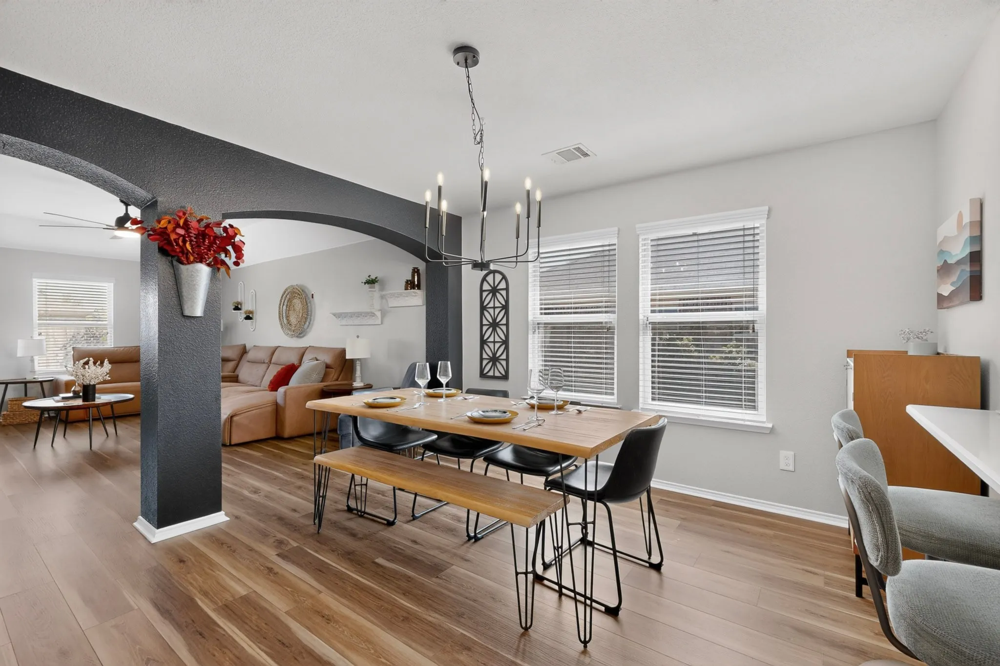 Wood-finish flooring throughout, archways defining spaces, two windows with blinds, and a contemporary chandelier