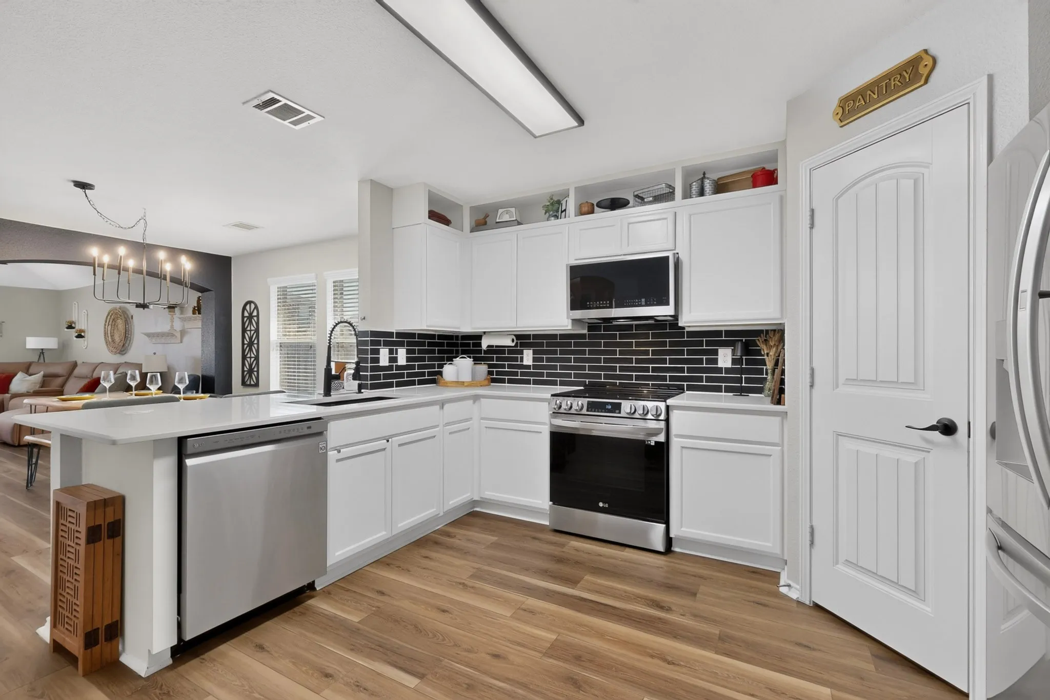 Contemporary kitchen featuring white cabinetry, stainless steel appliances, dark subway tile backsplash, white countertops, and wood-finish flooring