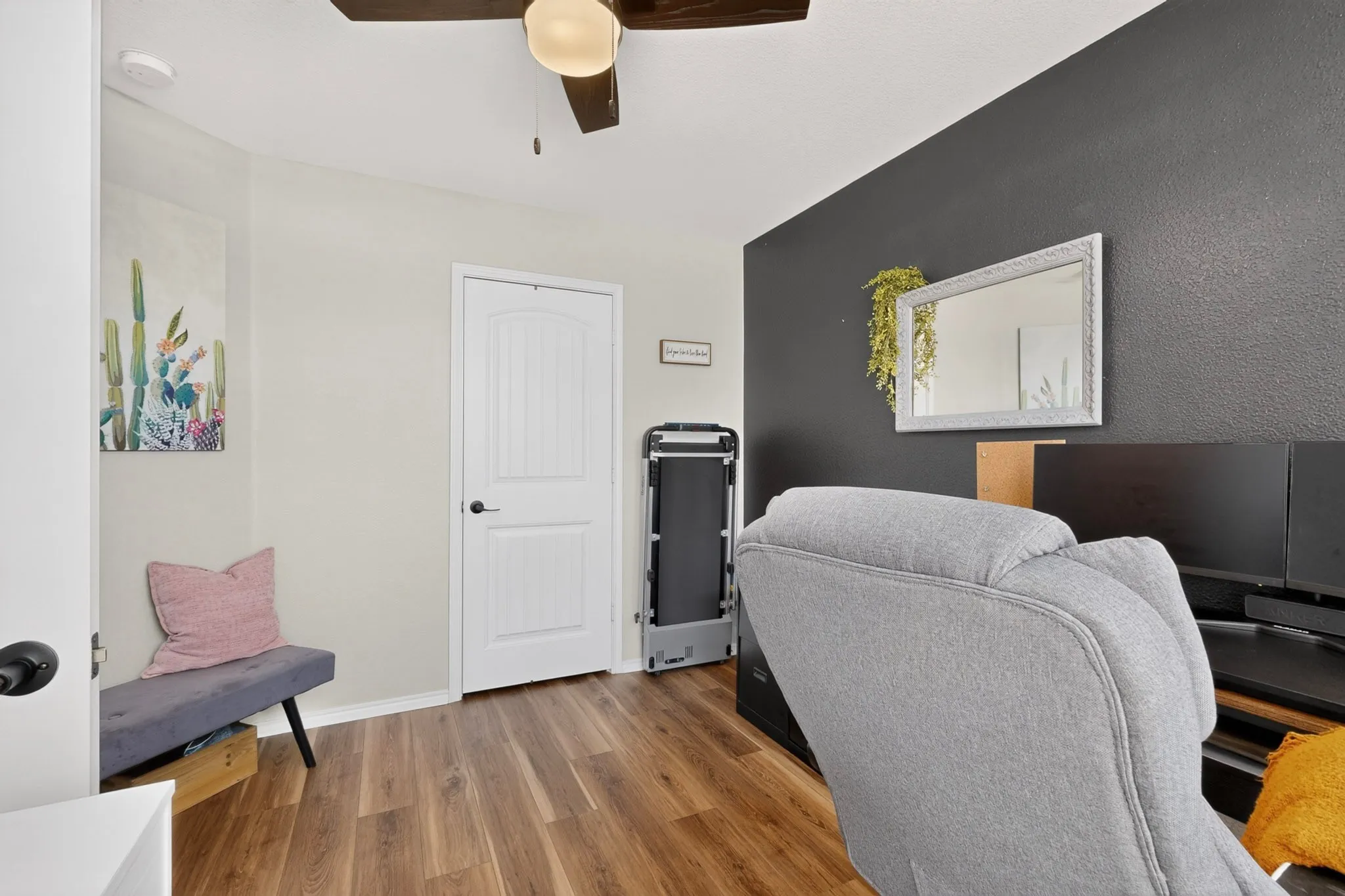 Wood-finish flooring, ceiling fan, white paneled interior door, and contrasting accent wall