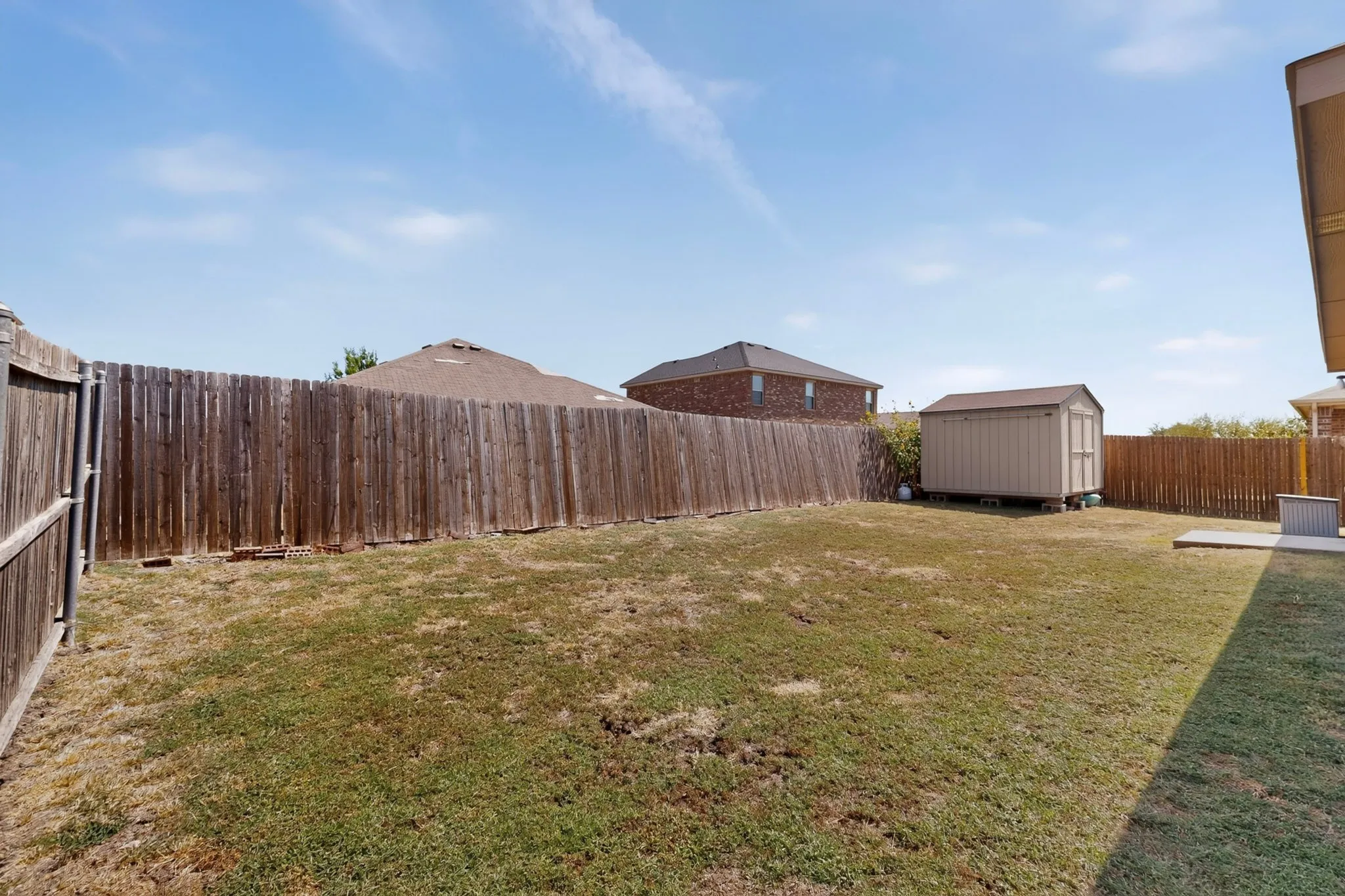 Expansive backyard featuring a privacy fence, detached storage shed, and a concrete patio